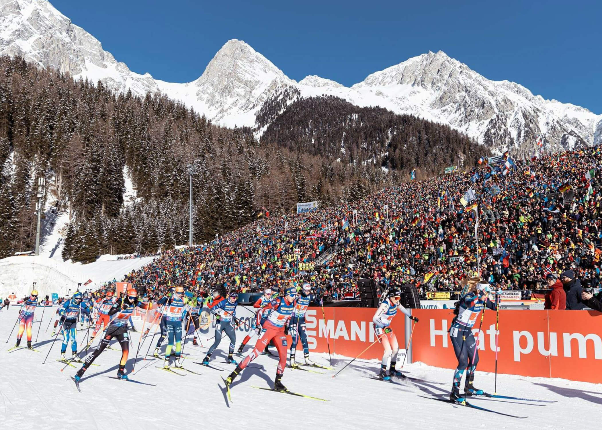 Biathlon-Skifahrer beim Rennen in den verschneiten Bergen mit einer großen Zuschauermenge im Hintergrund. - Hotel La Casies Mountain Living