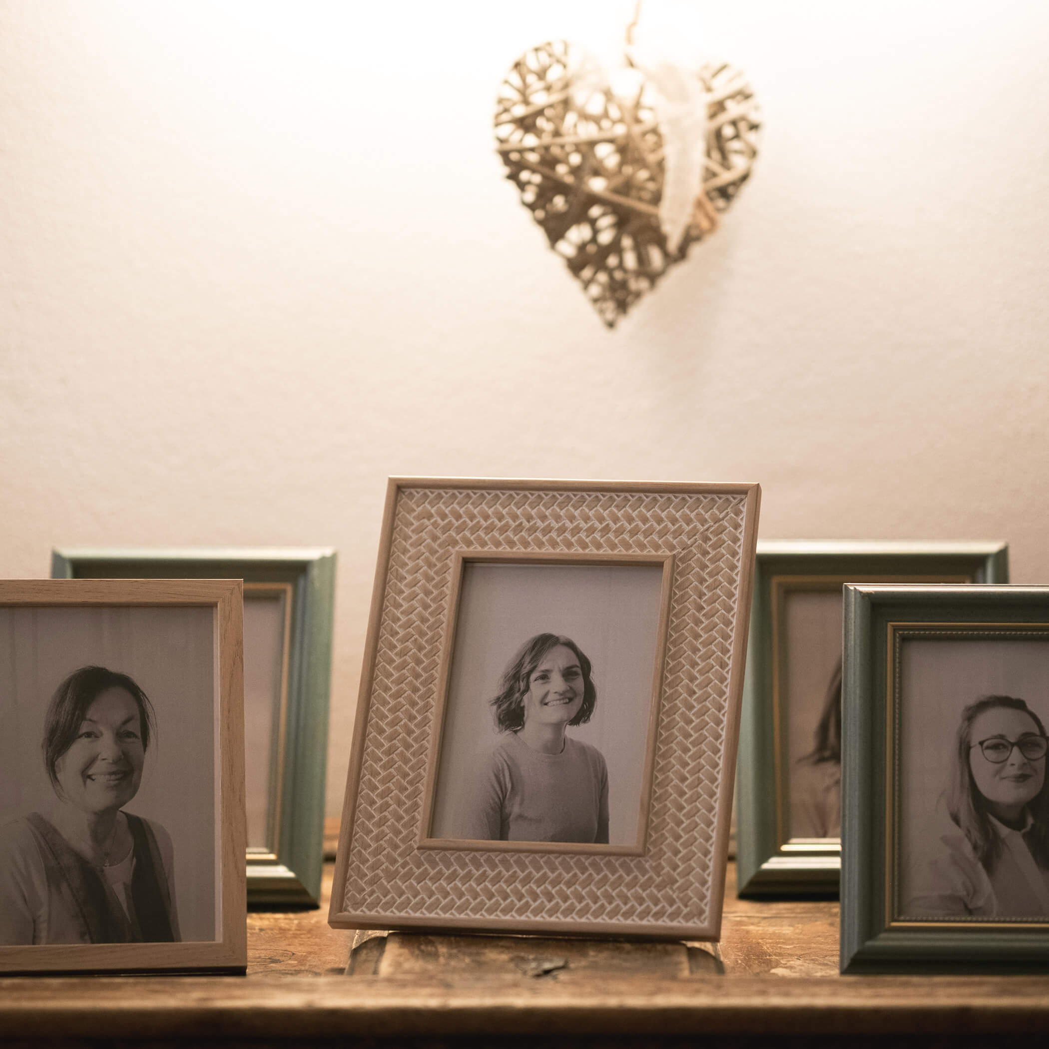 Fünf gerahmte Schwarz-Weiß-Porträts auf einem Tisch, darüber ein Weidenherz an der Wand. - Hotel La Casies Mountain Living