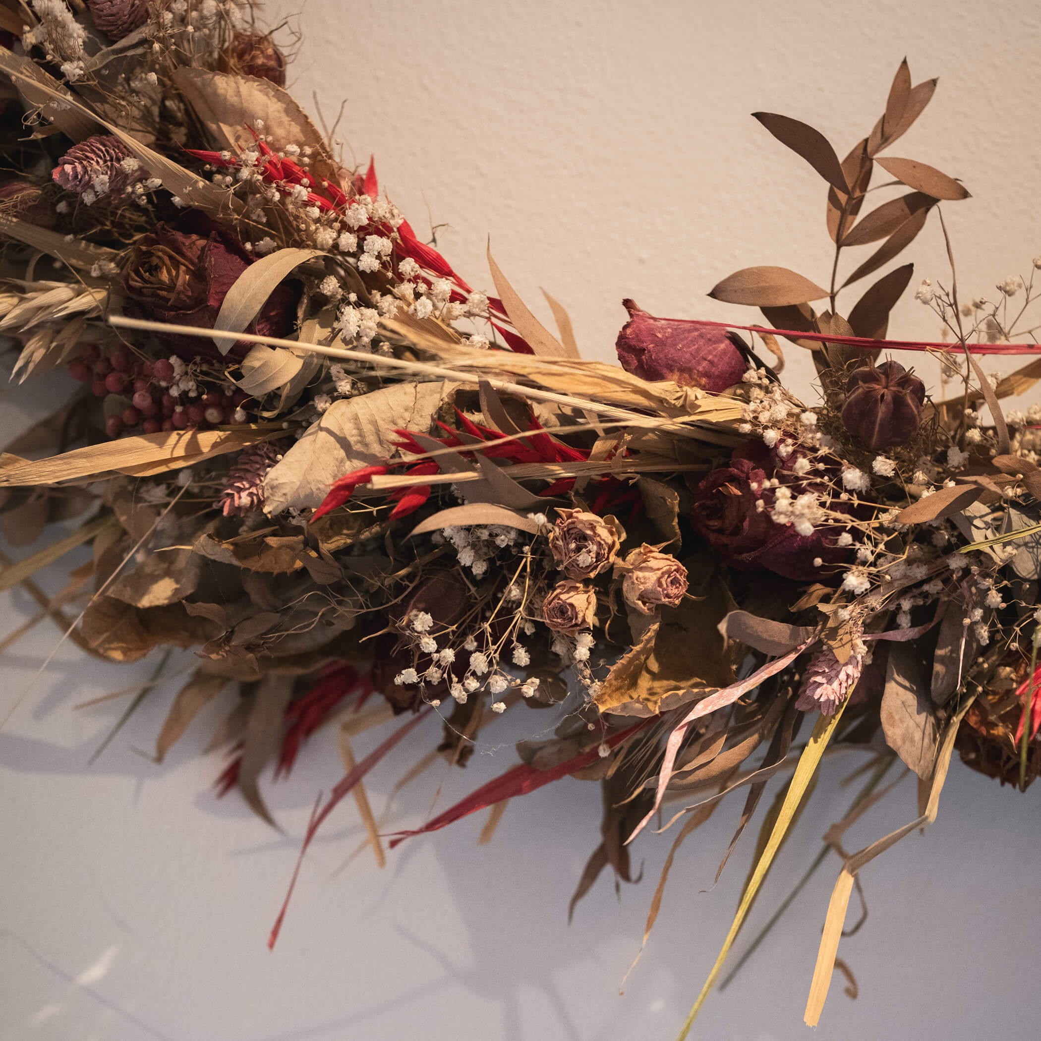 Eine Nahaufnahme eines getrockneten Blumenkranzes mit braunen Blättern, roten Blüten und weißem Schleierkraut. - Hotel La Casies Mountain Living
