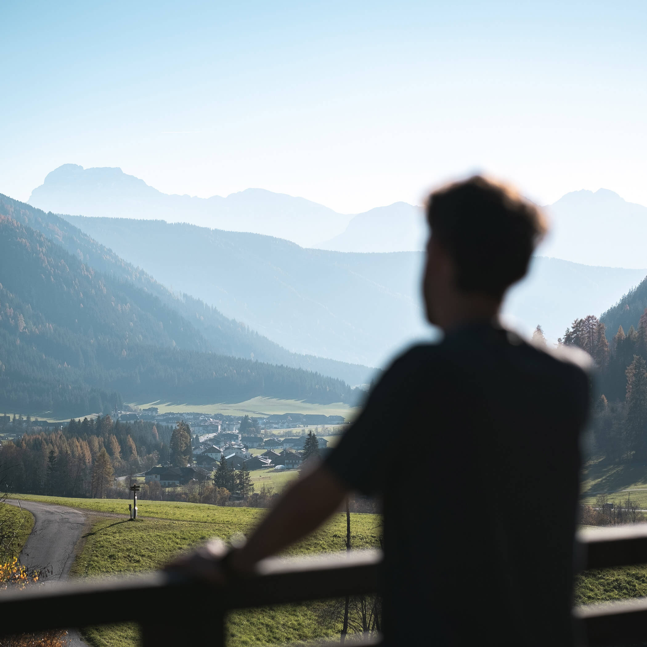 Eine Person blickt auf ein malerisches Tal mit Bergen und einem kleinen Dorf in der Ferne. - Hotel La Casies Mountain Living