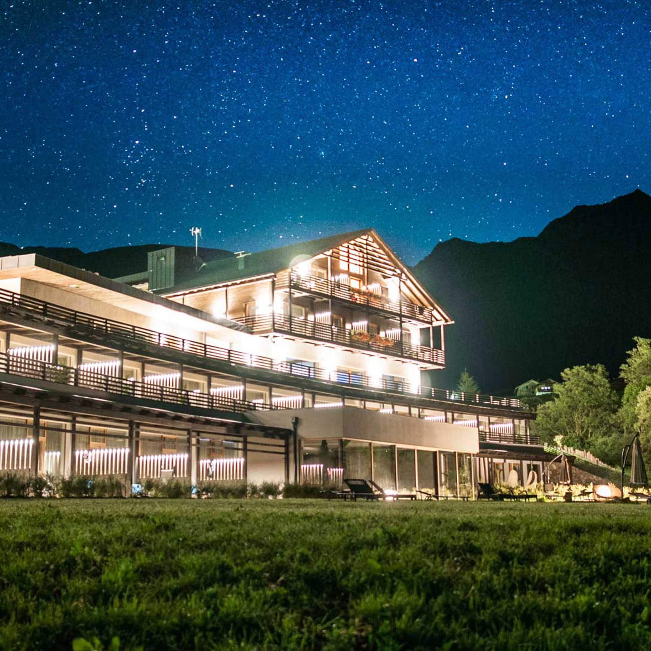 Eine hell erleuchtete, moderne Lodge unter einem klaren Sternenhimmel, mit den Bergen im Hintergrund als Silhouette. - Hotel La Casies Mountain Living