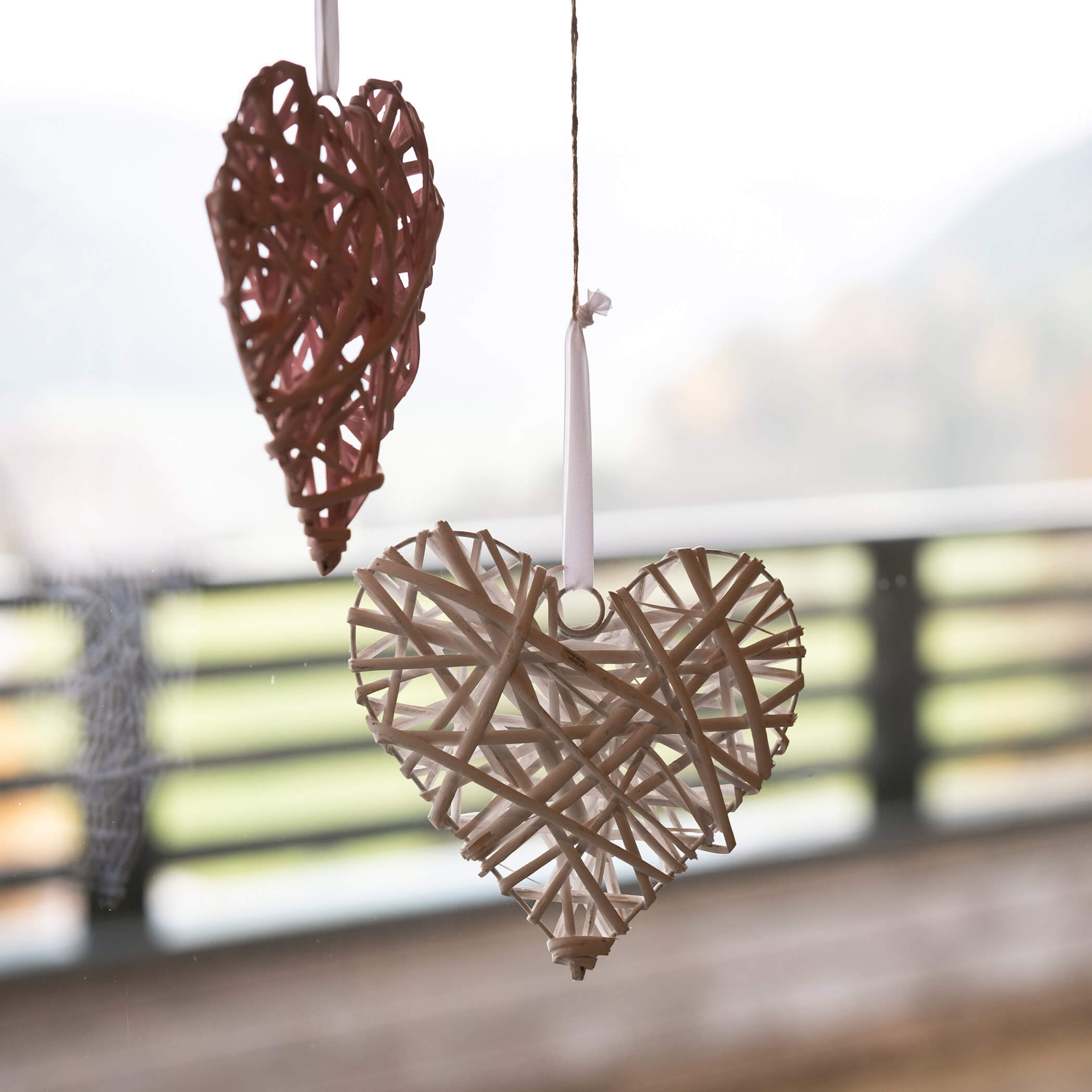 Zwei gewebte Herz-Ornamente hängen an Bändern vor einem unscharfen Hintergrund im Freien. - Hotel La Casies Mountain Living