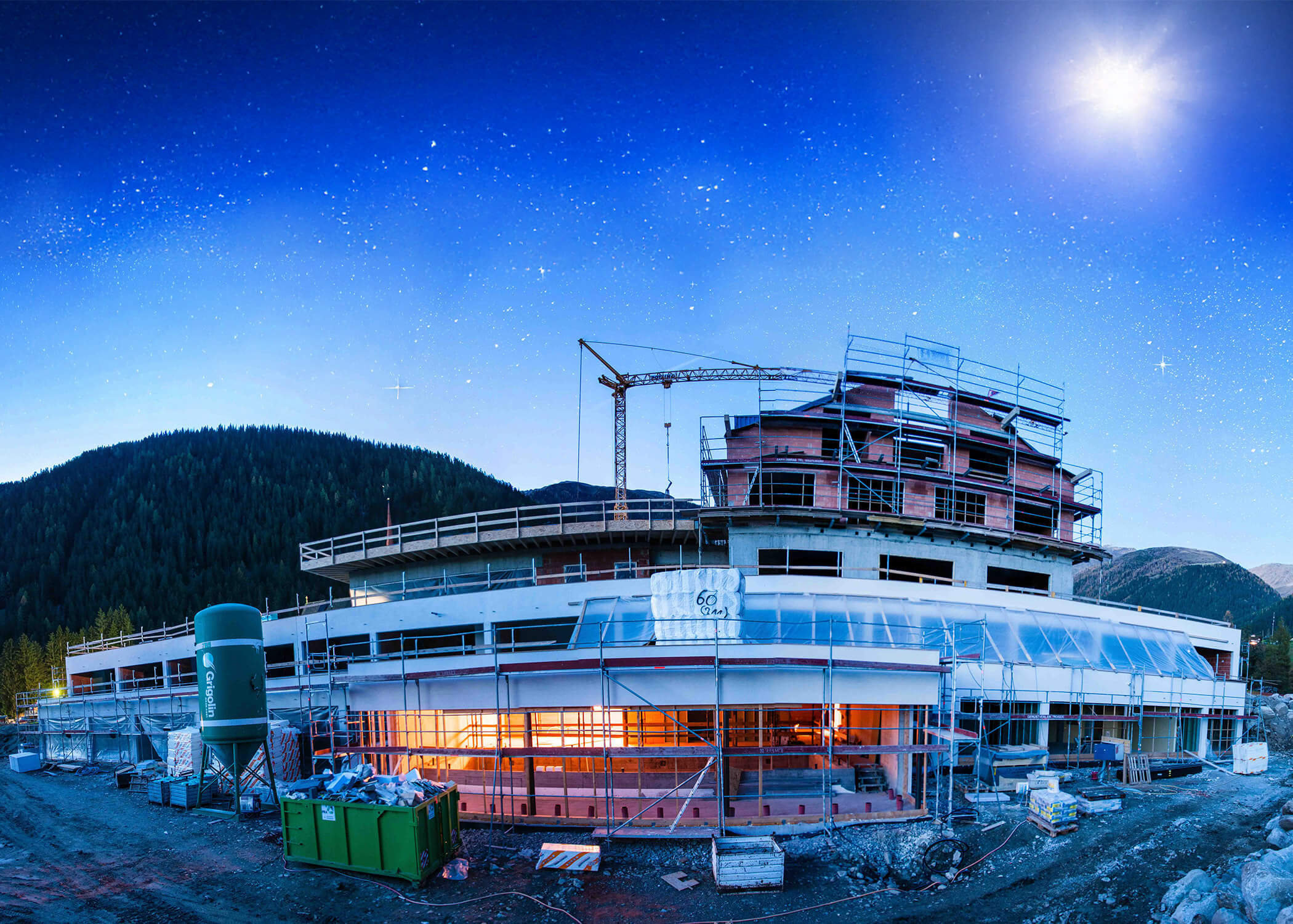 Ein modernes Gebäude im Bau in der Abenddämmerung, mit einem Kran, Bergen und einem Sternenhimmel im Hintergrund. - Hotel La Casies Mountain Living