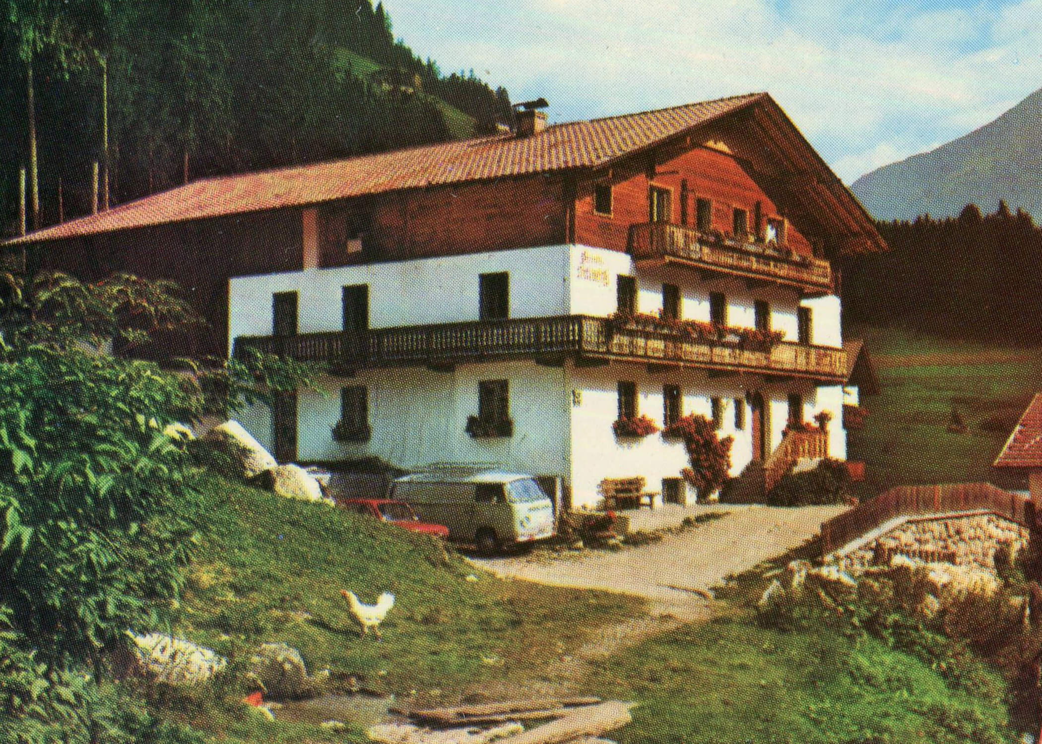Ein rustikales Chalet mit Blumenkästen, einem Lieferwagen und einem Huhn inmitten einer Berglandschaft. - Hotel La Casies Mountain Living