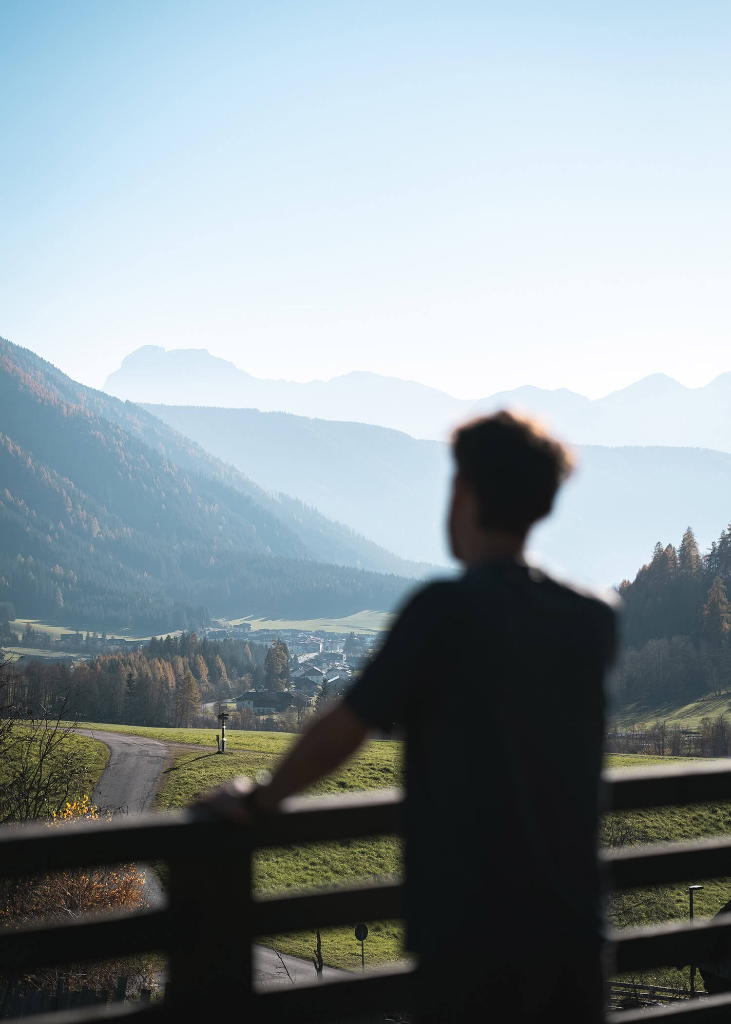 A person stands on a balcony overlooking a scenic valley with mountains and greenery in the distance. - Hotel La Casies Mountain Living