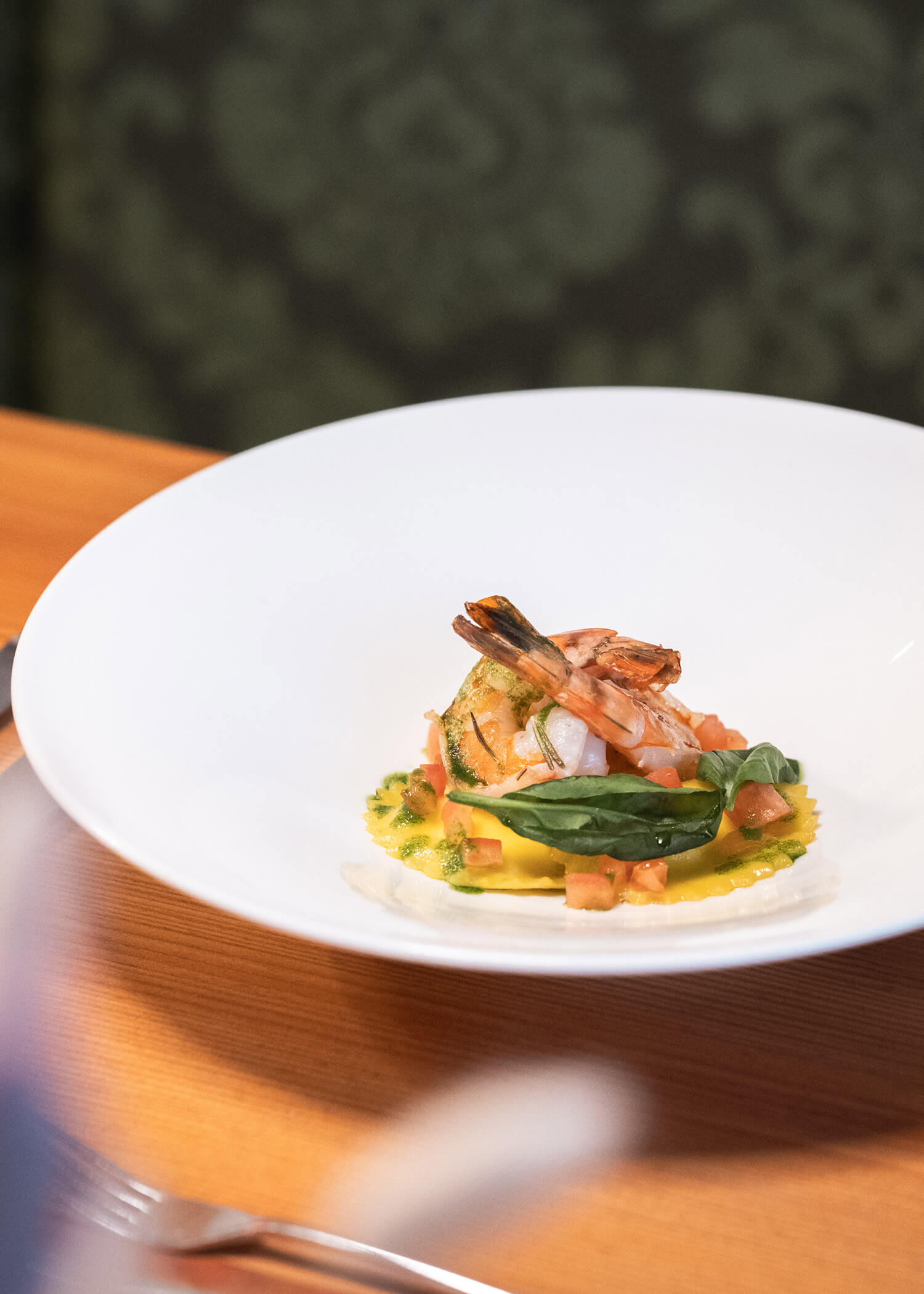 Shrimp atop ravioli with diced tomatoes and greens, artfully plated on a white dish. - Hotel La Casies Mountain Living