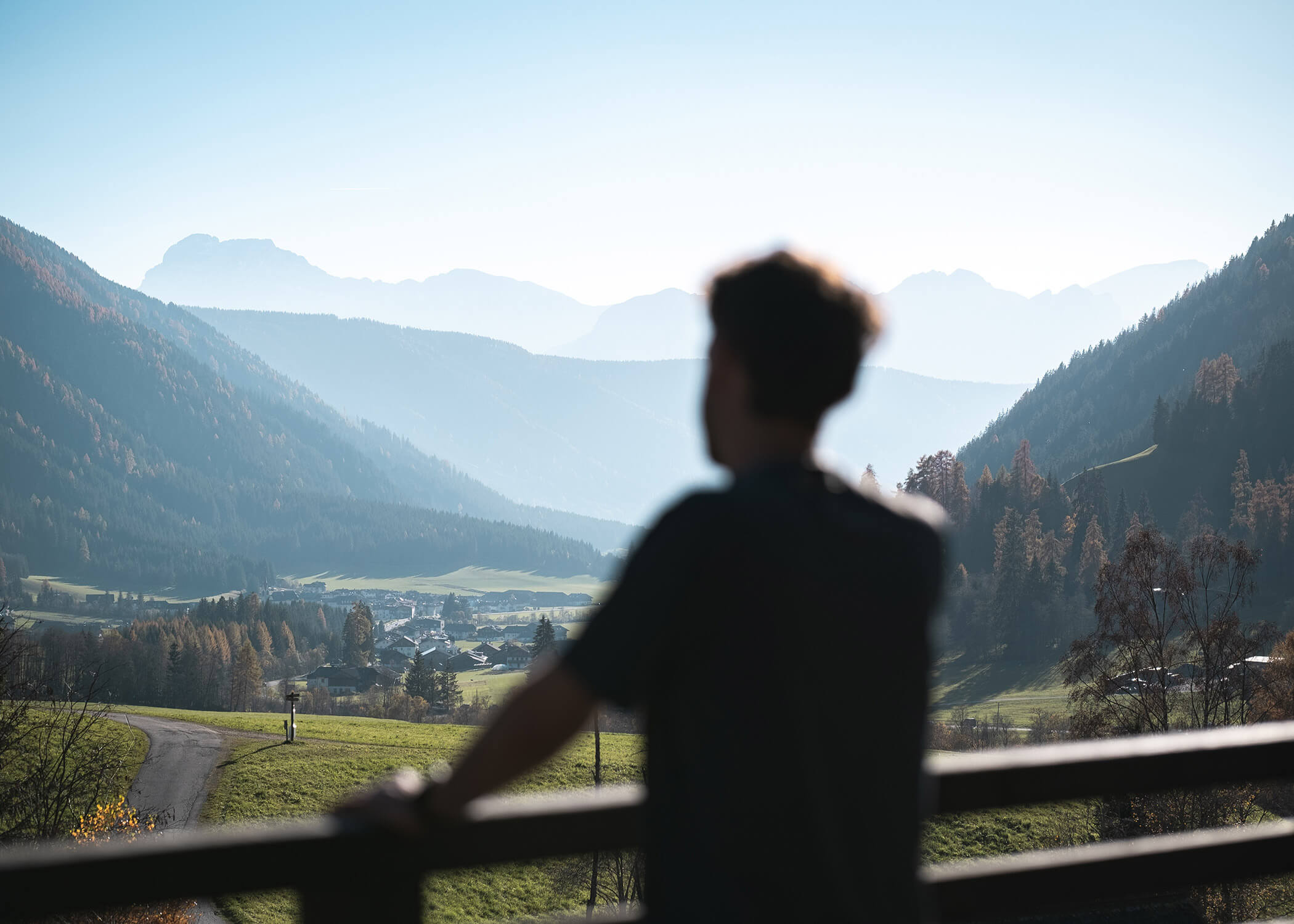 Eine Person steht auf einem Balkon und blickt auf ein malerisches Tal mit Bergen in der Ferne. - Hotel La Casies Mountain Living