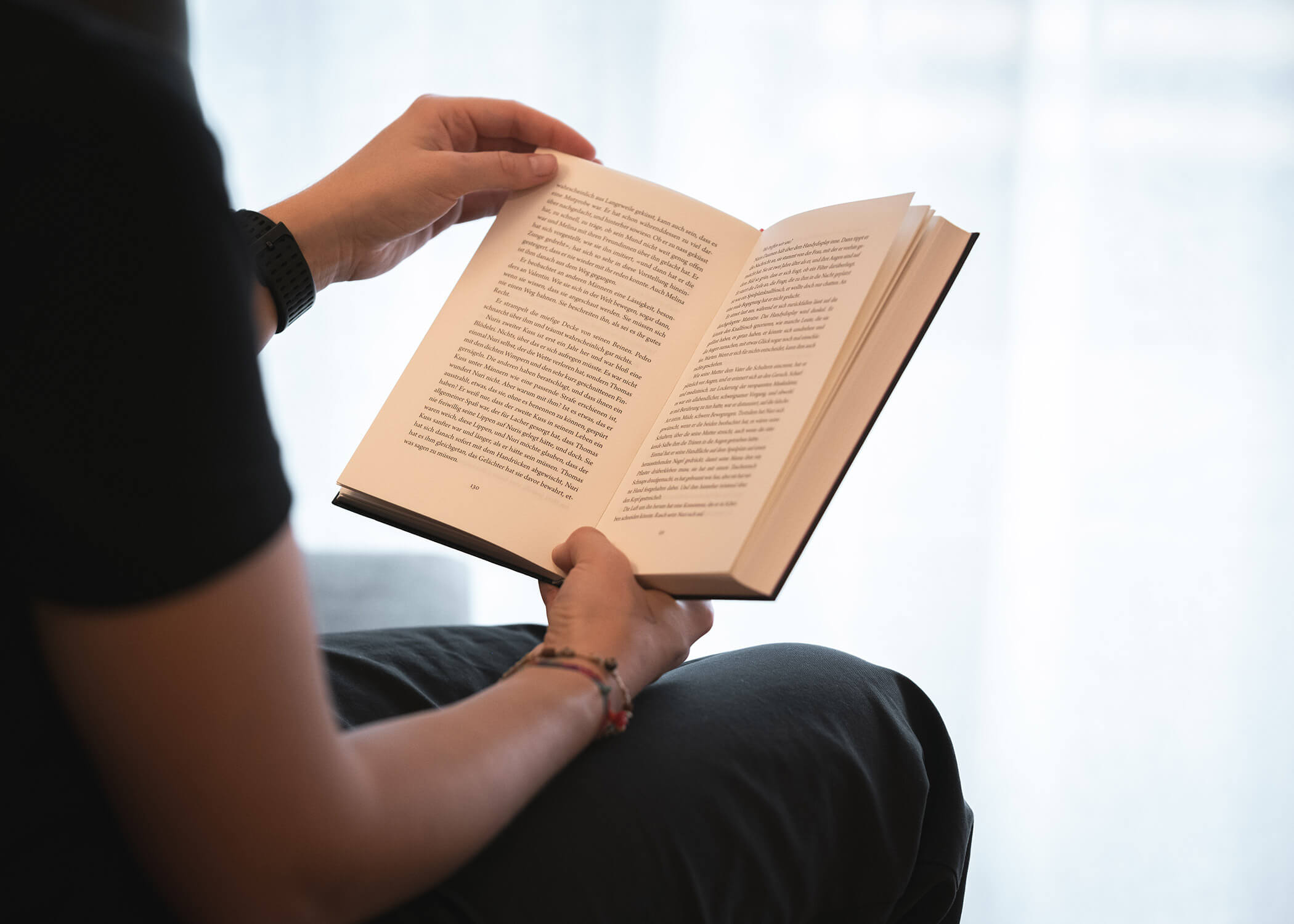 Sitzende Person, die ein aufgeschlagenes Buch liest und es mit beiden Händen in der Nähe eines hellen Fensters hält. - Hotel La Casies Mountain Living