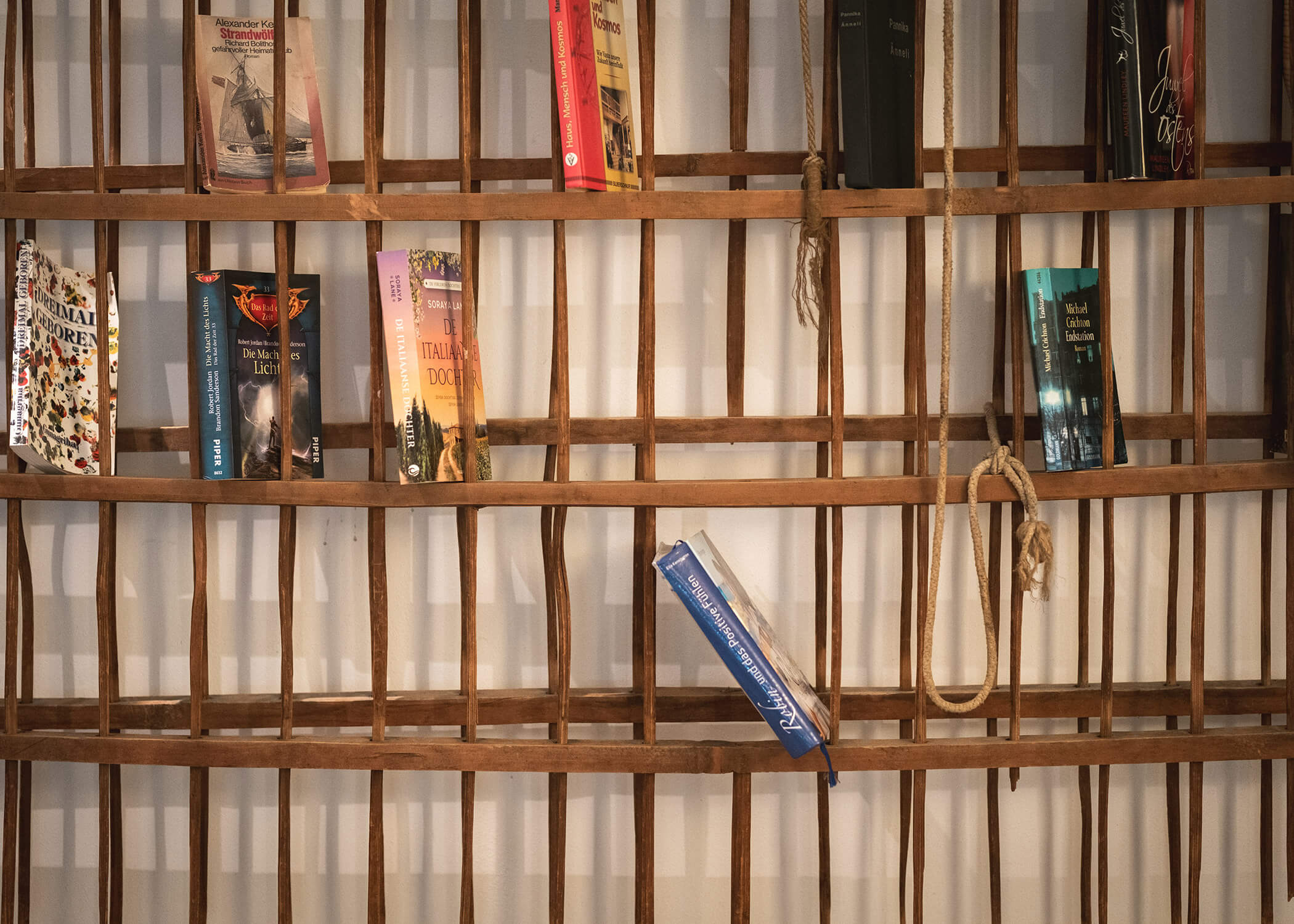 Die Bücher sind auf einem mit Seilen versehenen Holzregal in Form eines Gitters ausgestellt, wobei einige schief und schräg stehen. - Hotel La Casies Mountain Living