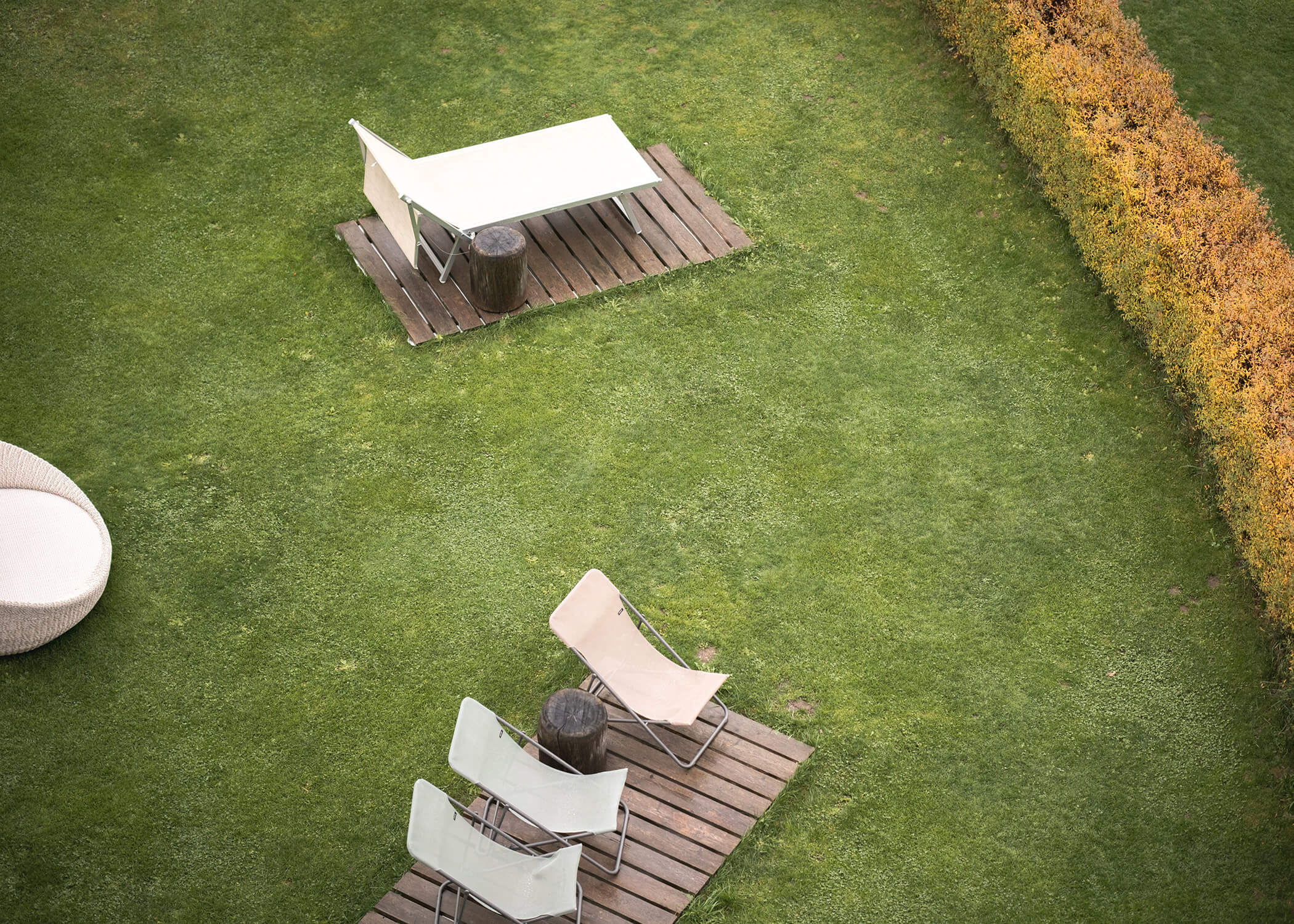 Luftaufnahme von Liegestühlen und Tischen im Freien auf einer Rasenfläche mit einer Hecke an einer Seite. - Hotel La Casies Mountain Living