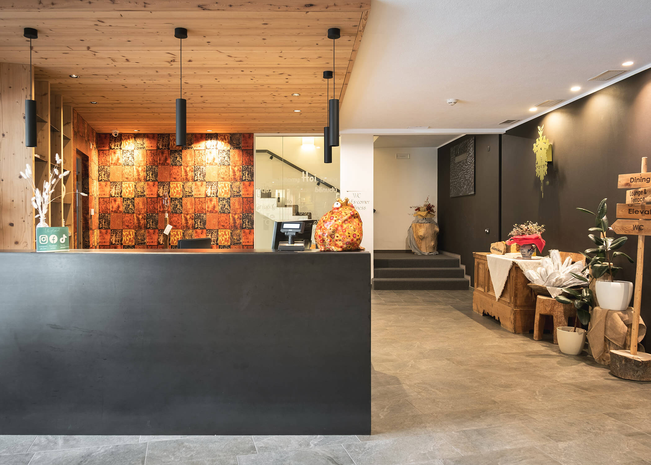 Moderne Hotelrezeption mit schwarzem Schreibtisch, warmer Beleuchtung und rustikalen Holzdekor-Akzenten. - Hotel La Casies Mountain Living