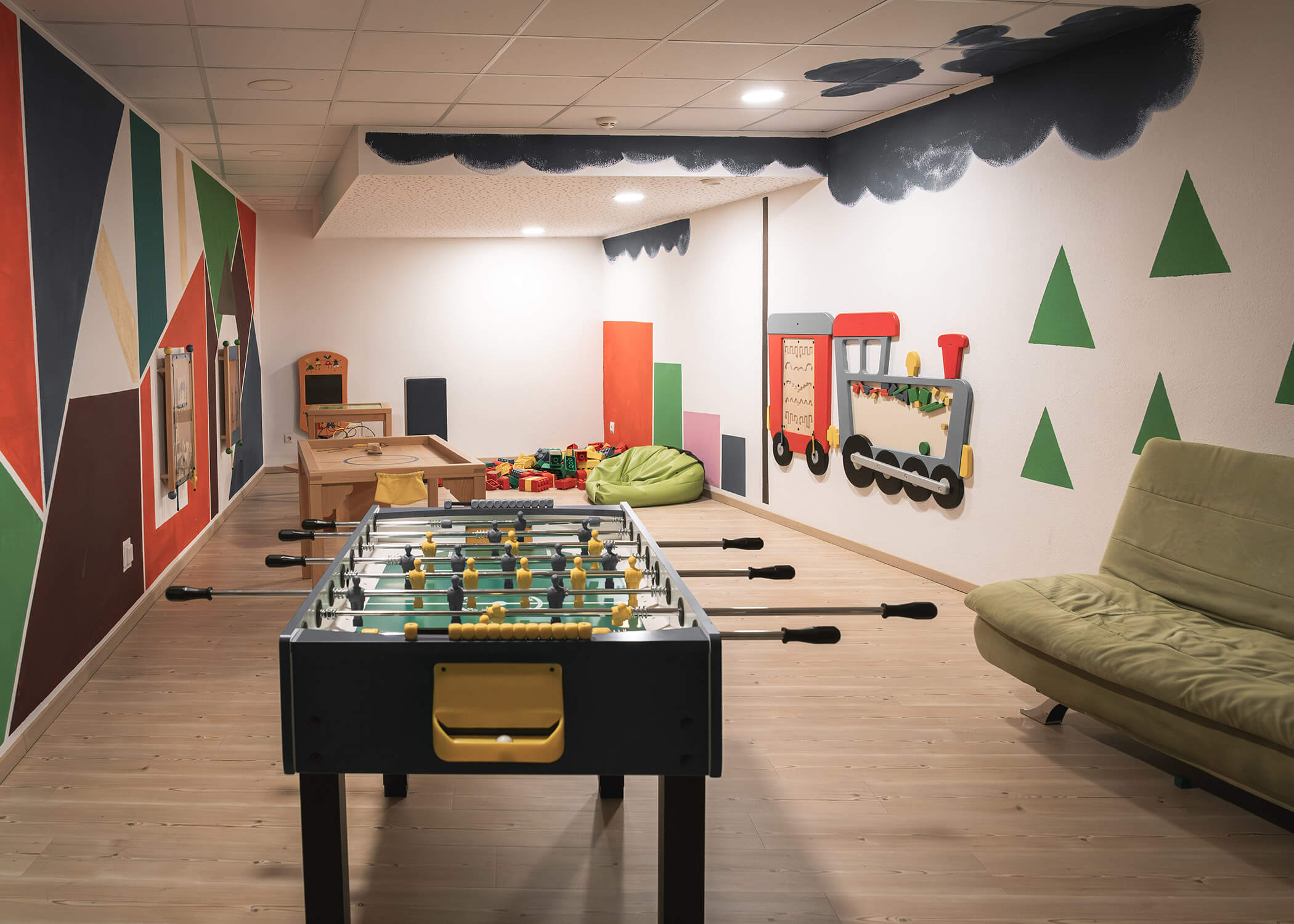 Ein farbenfrohes Spielzimmer mit einem Kickertisch, Spielzeug, Wandkunst, grünen Sitzsäcken und einem grünen Sofa. - Hotel La Casies Mountain Living