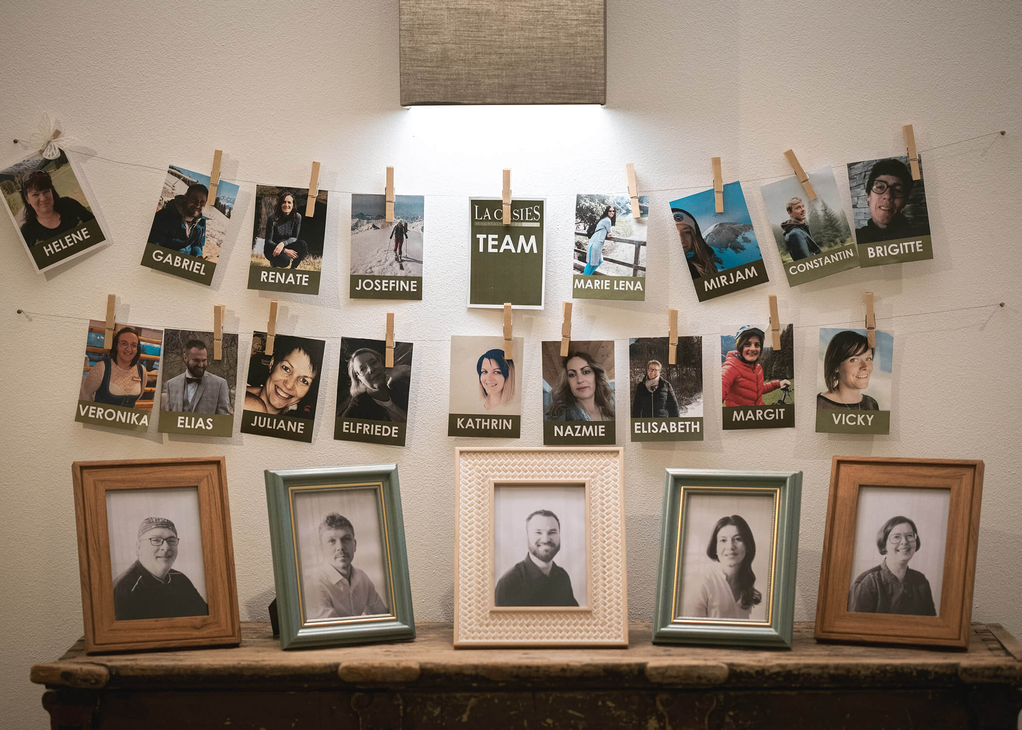 Fotos von Menschen, einige in Farbe und einige in Schwarz-Weiß, an einer Wand mit Namensschildern und Rahmen. - Hotel La Casies Mountain Living