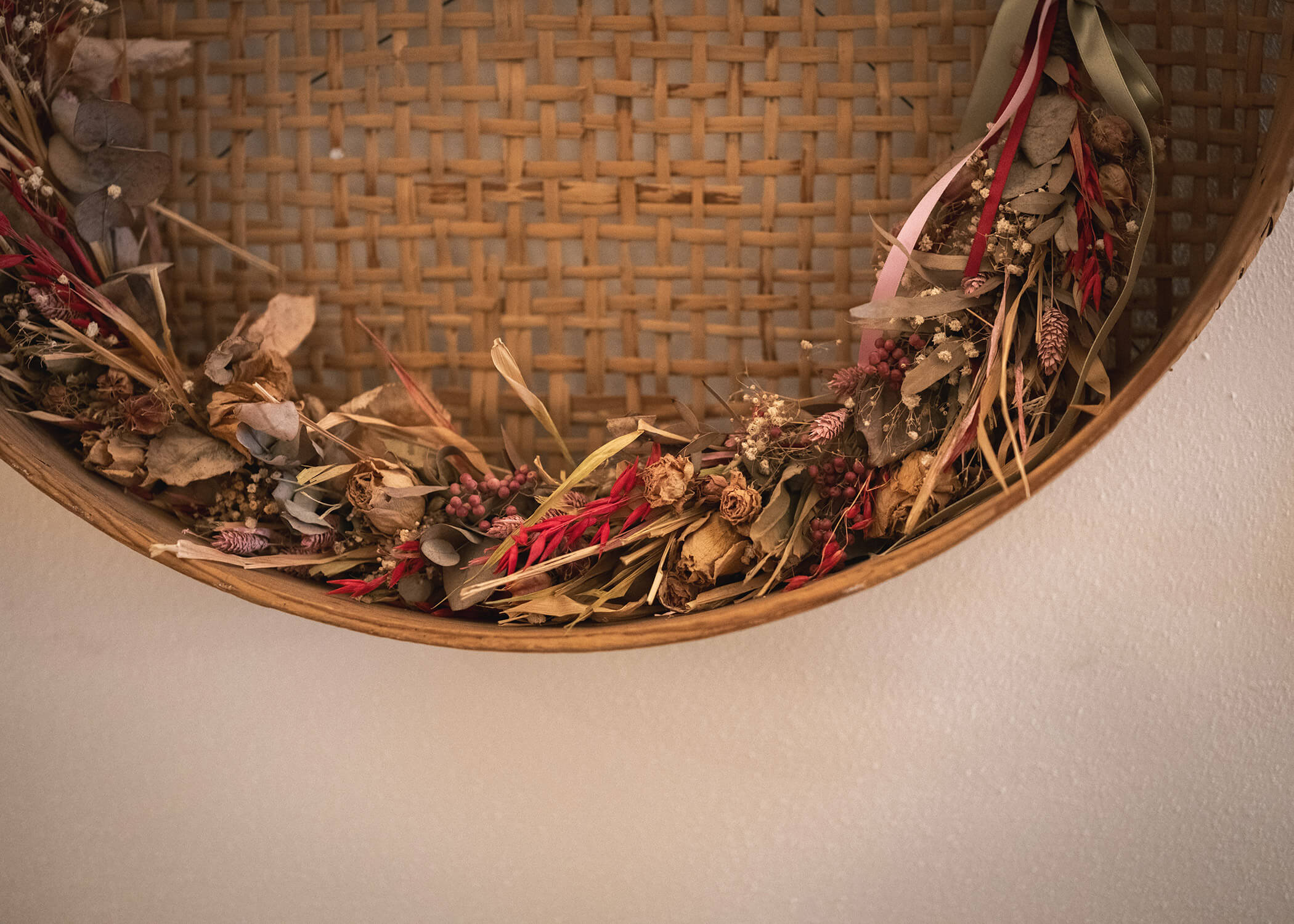 Ein geflochtener Korb mit getrockneten Blumen und Gräsern, der an einer beigen Wand hängt. - Hotel La Casies Mountain Living