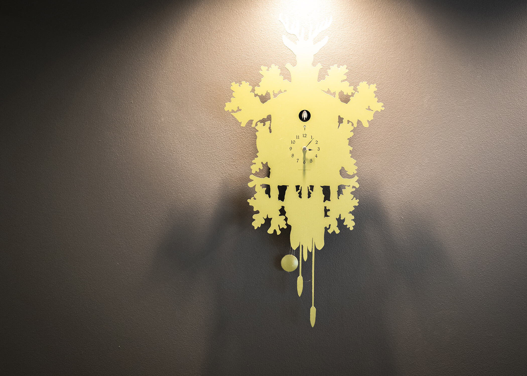 Gelbe dekorative Uhr mit kompliziertem Muster auf einer grauen Wand, von oben beleuchtet. - Hotel La Casies Mountain Living