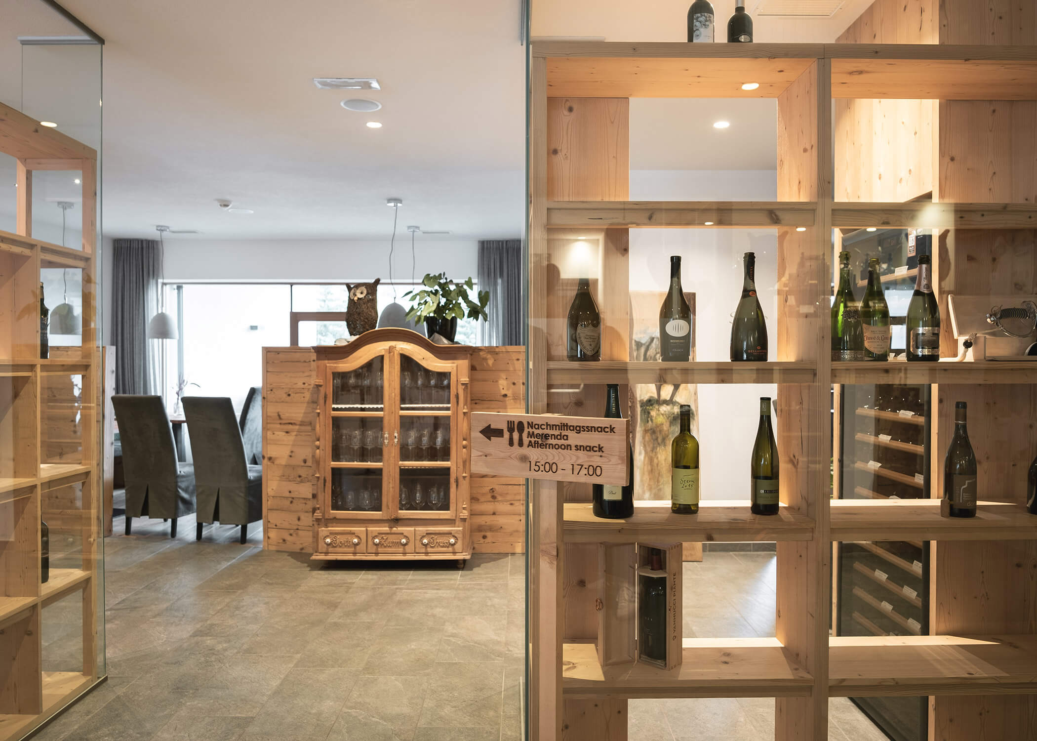 Weinregale aus Holz mit Flaschen neben einem Essbereich mit Schrank und Stühlen in einem modernen Raum. - Hotel La Casies Mountain Living