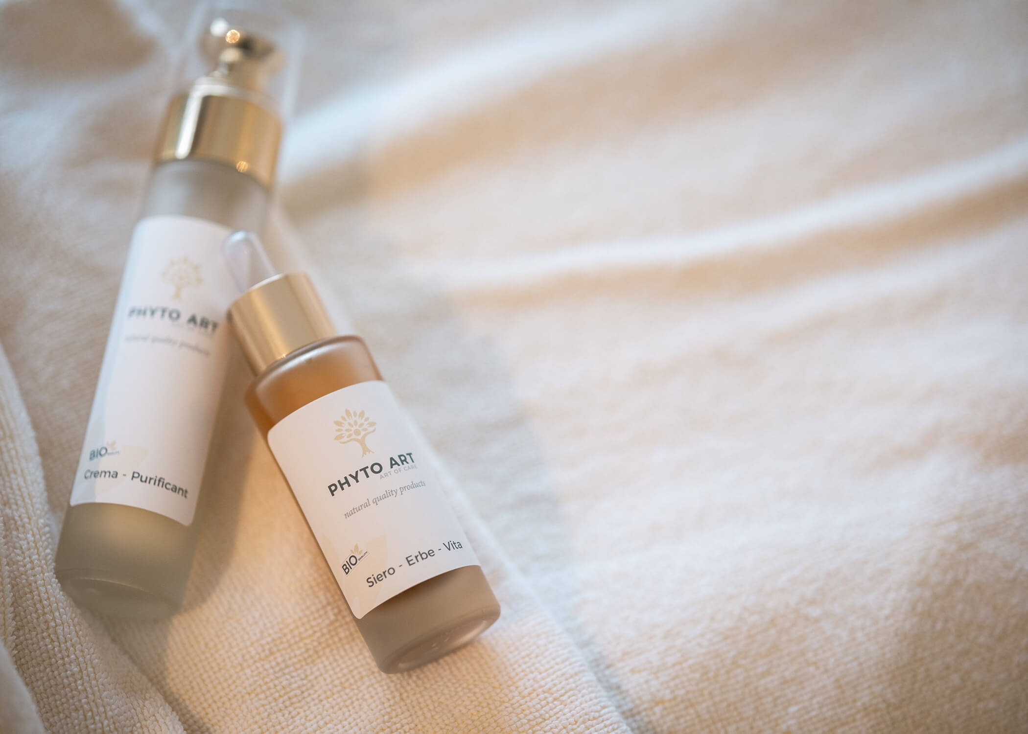 Zwei Hautpflegeflaschen mit der Aufschrift PHYTO ART auf einem weißen, strukturierten Handtuch. - Hotel La Casies Mountain Living