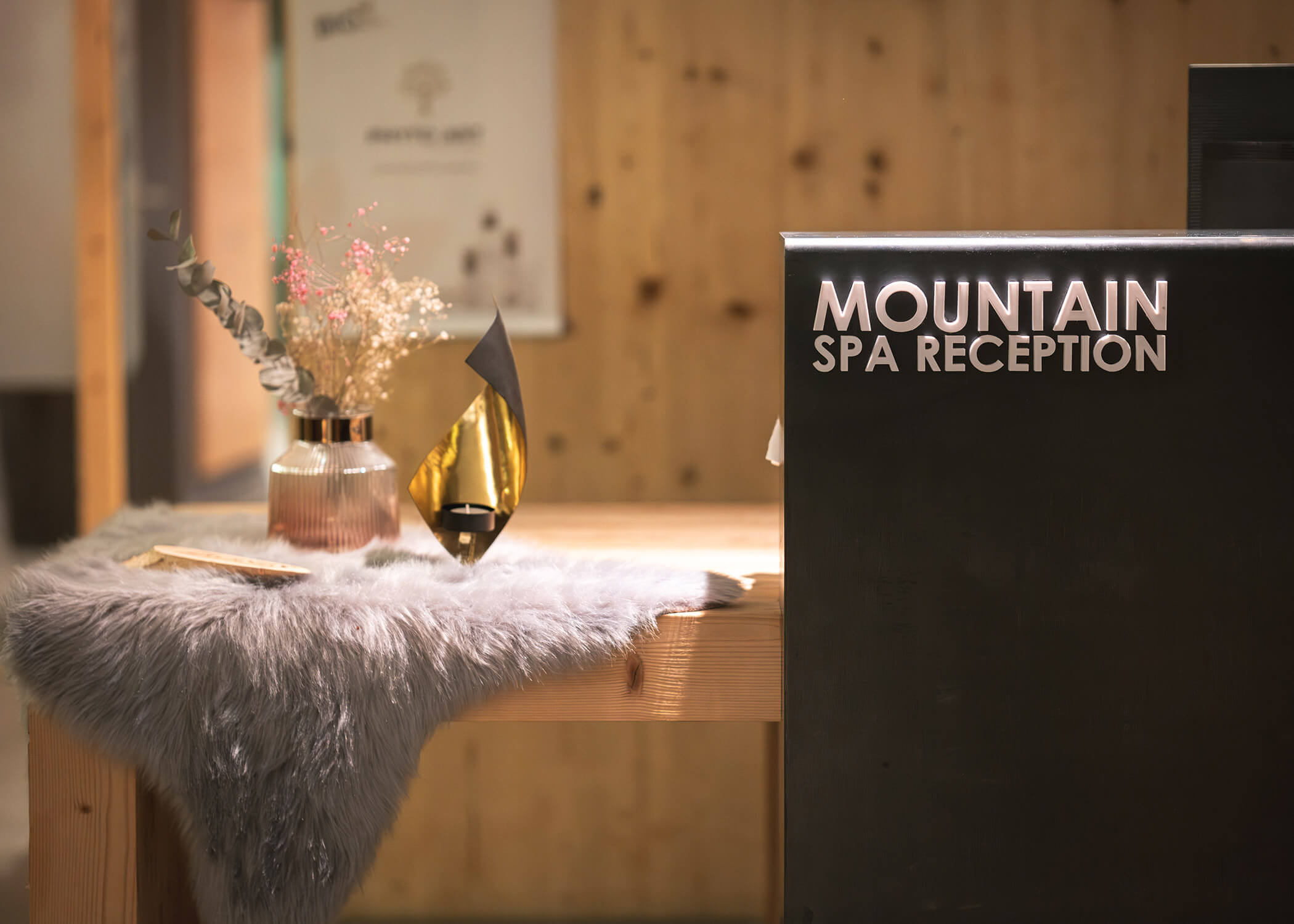 Empfangstisch mit Mountain Spa Reception-Schild, Pelzläufer, Vase, Trockenblumen und modernem Dekor. - Hotel La Casies Mountain Living