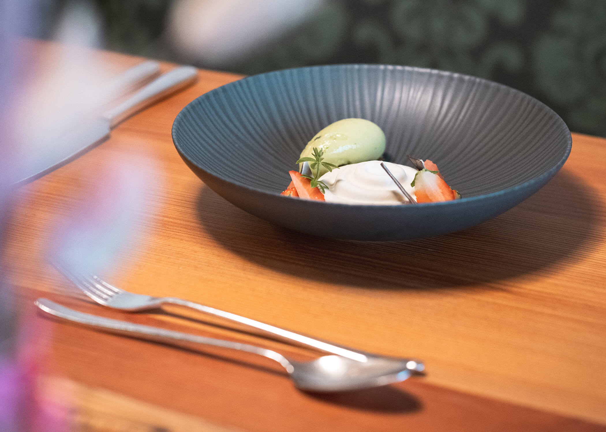 Ein Dessert mit grünem Eis, Sahne und Erdbeeren in einer schwarzen Schale auf einem Holztisch. - Hotel La Casies Mountain Living