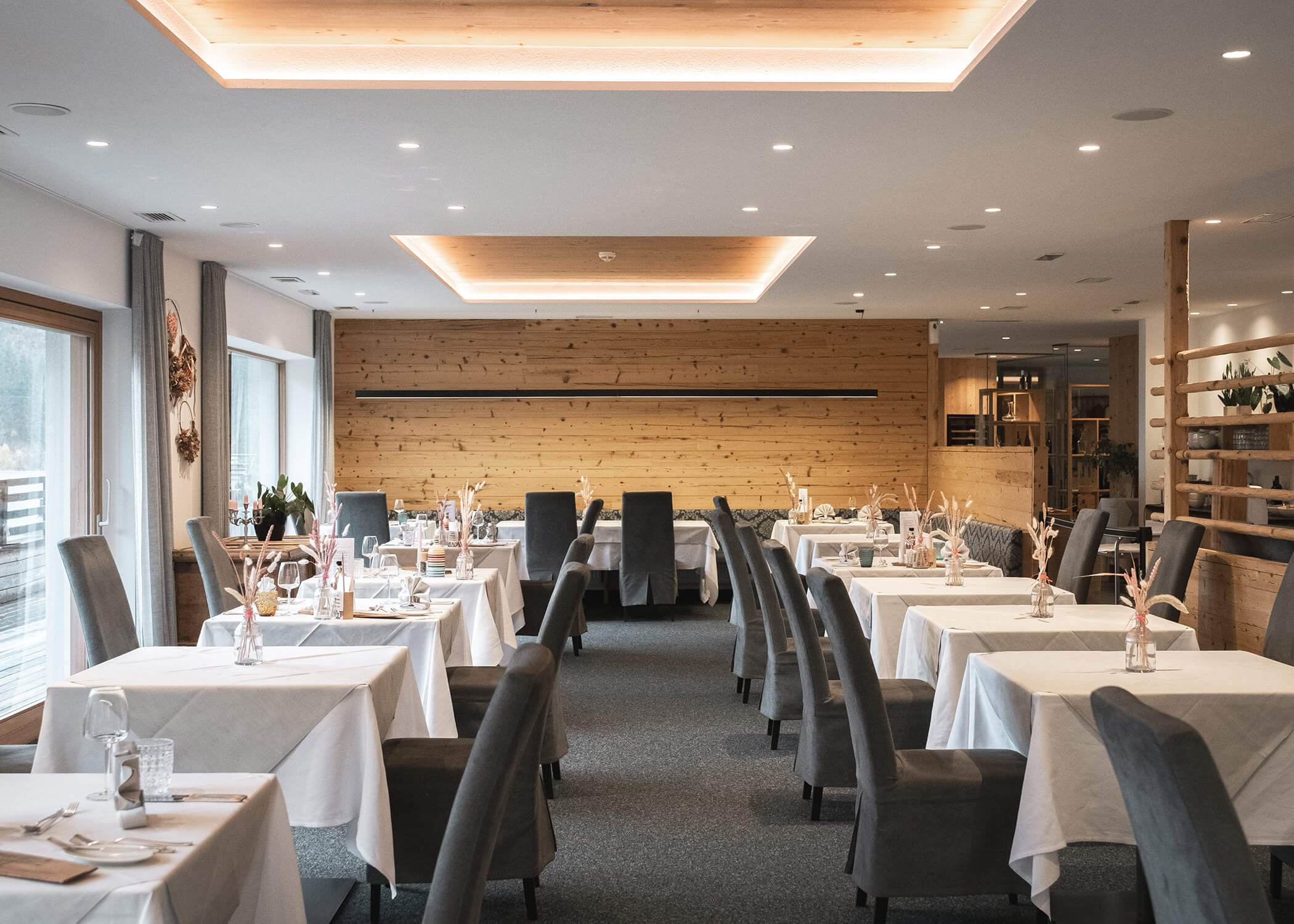 Moderner Speisesaal eines Restaurants mit grauen Stühlen, weißen Tischdecken und hölzernen Akzenten, gedämpftes Licht. - Hotel La Casies Mountain Living