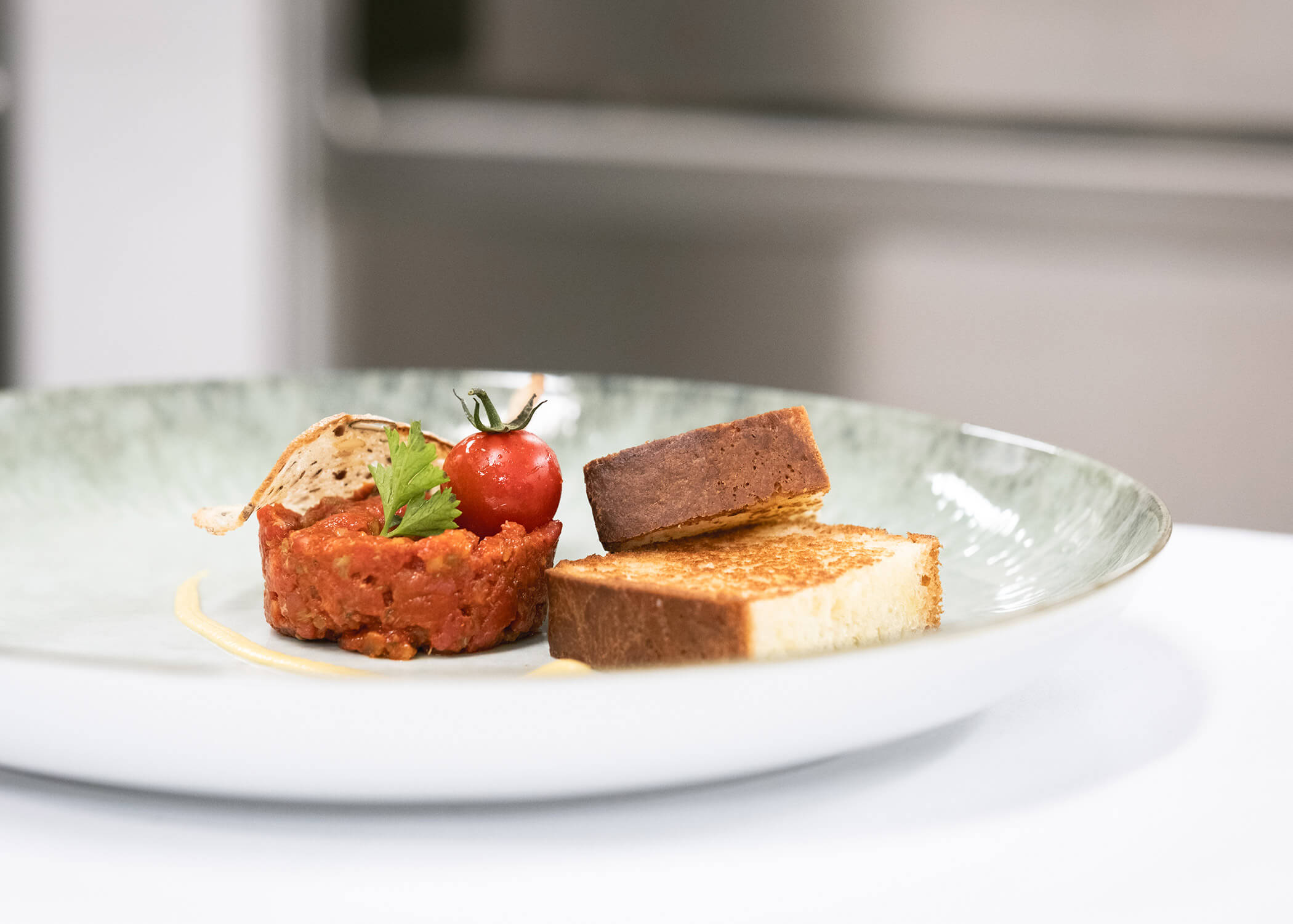 Eine plattierte Vorspeise mit Steak-Tartar, Toastscheiben, einer Kirschtomate und einem knusprigen Brotchip auf einem weißen Teller. - Hotel La Casies Mountain Living