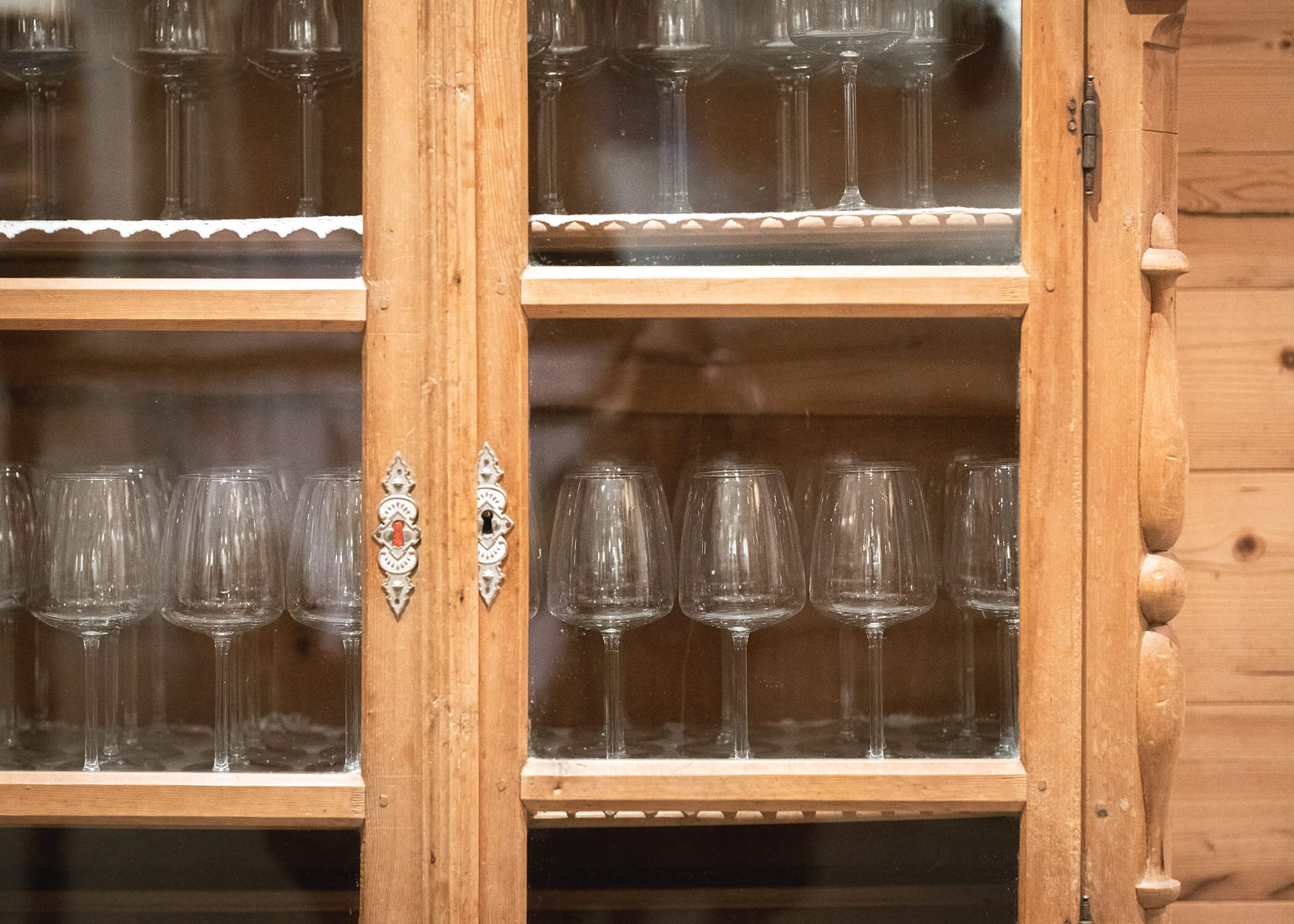 Holzschrank mit Glastüren, in dessen Regalen Reihen von leeren Weingläsern stehen. - Hotel La Casies Mountain Living