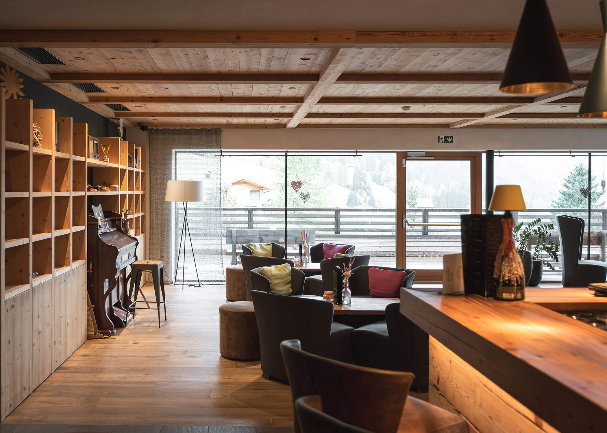 Gemütlicher Aufenthaltsraum mit Holzdekor, Sesseln, Regalen und großen Fenstern mit Blick auf die malerische Landschaft. - Hotel La Casies Mountain Living
