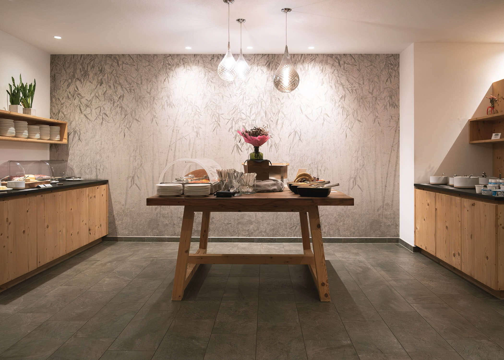 Frühstücksbuffet mit Gebäck, Tellern und Besteck auf einem Holztisch in einem modernen, hellen Raum. - Hotel La Casies Mountain Living