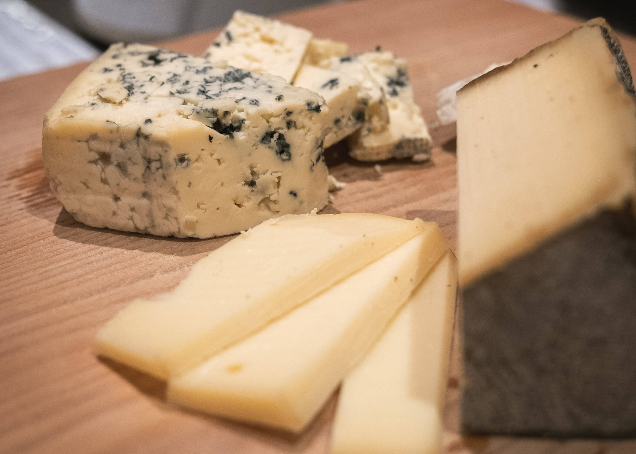 Nahaufnahme von verschiedenen Käsesorten, darunter Blauschimmelkäse und geschnittener Hartkäse, auf einem Holzbrett. - Hotel La Casies Mountain Living
