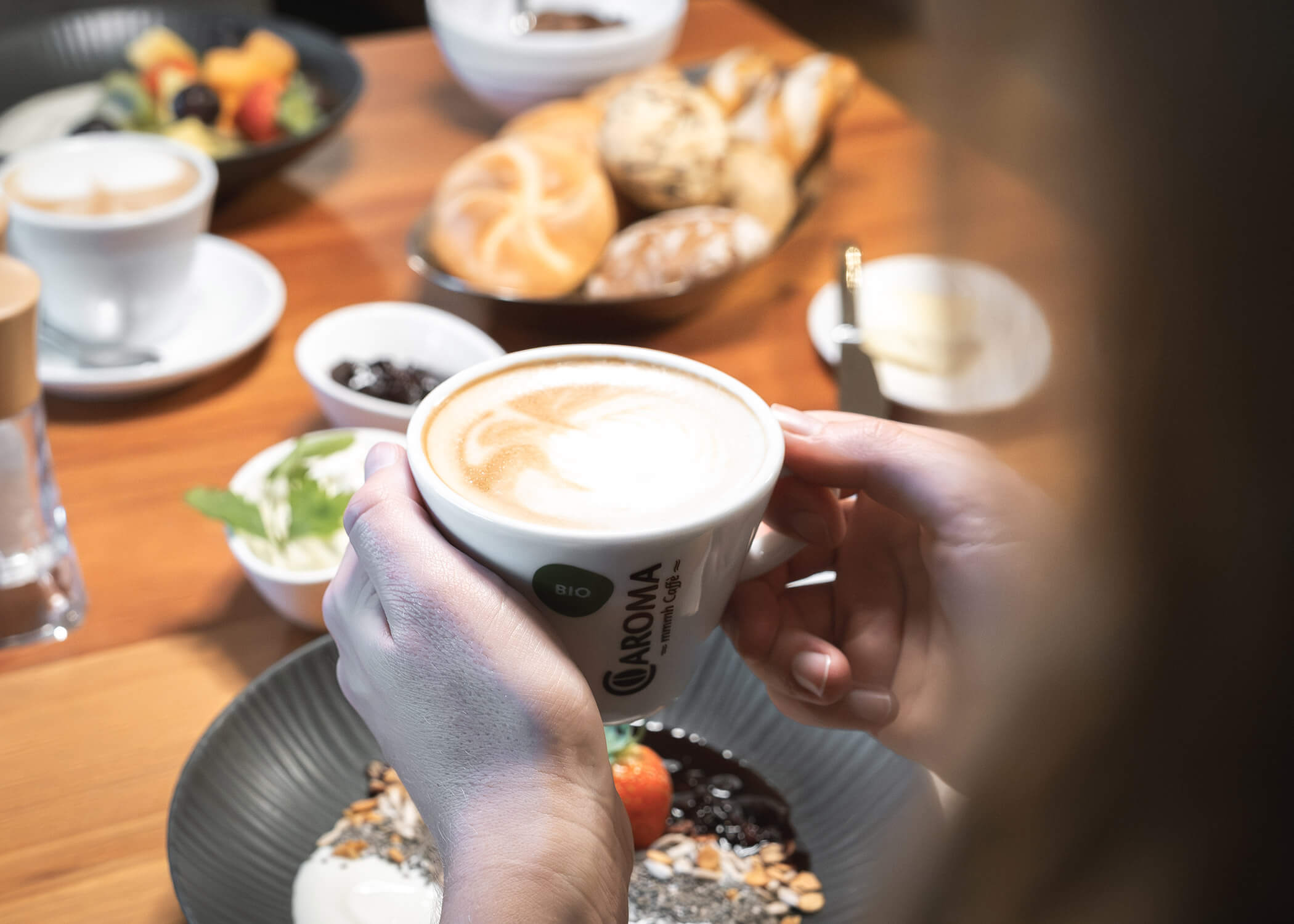 Eine Person hält eine Tasse Kaffee an einem Frühstückstisch mit Gebäck, Obst und kleinem Geschirr. - Hotel La Casies Mountain Living