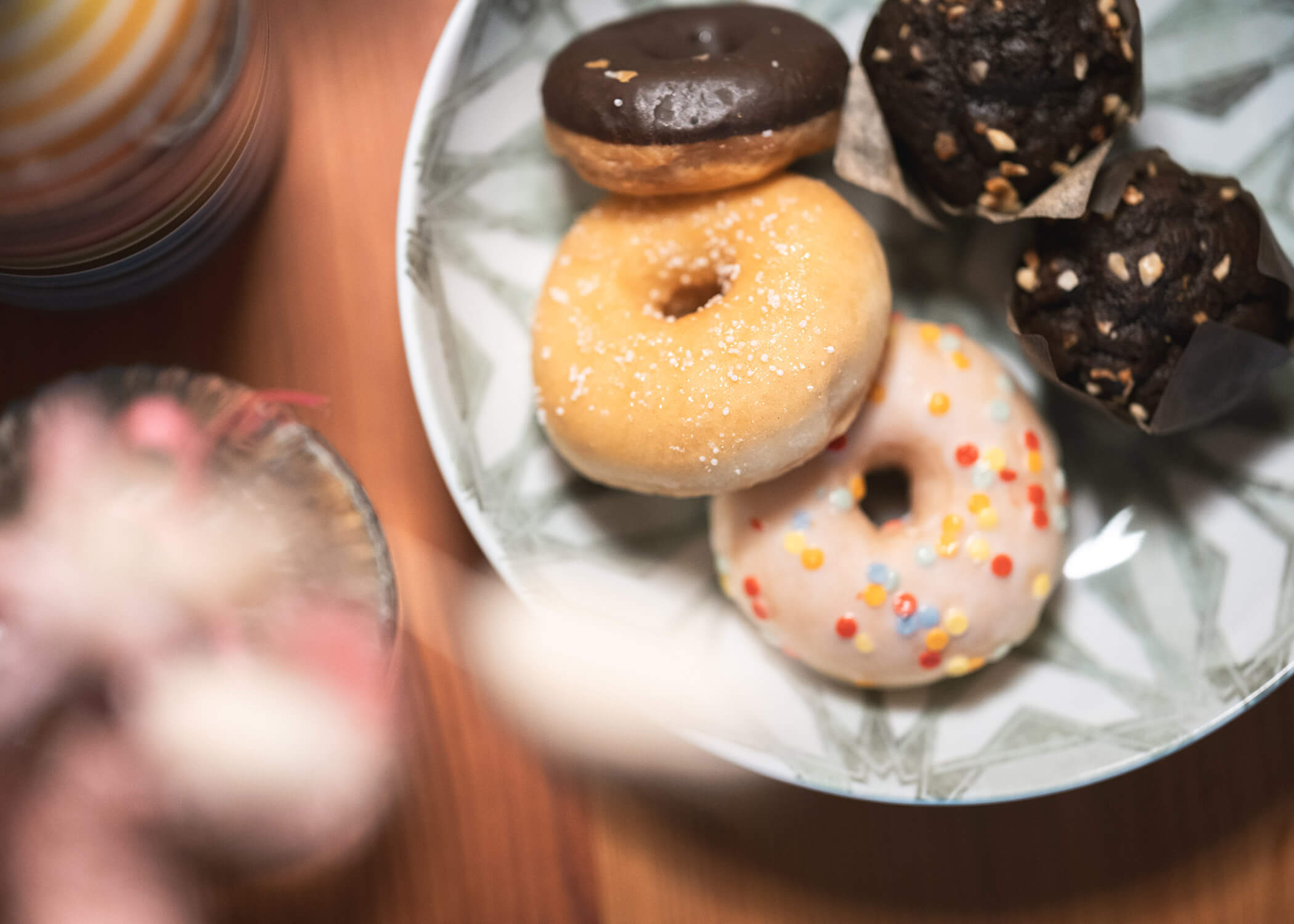 Ein Teller mit verschiedenen Donuts, darunter glasierte, schokolierte und bestreute, auf einem Holztisch. - Hotel La Casies Mountain Living