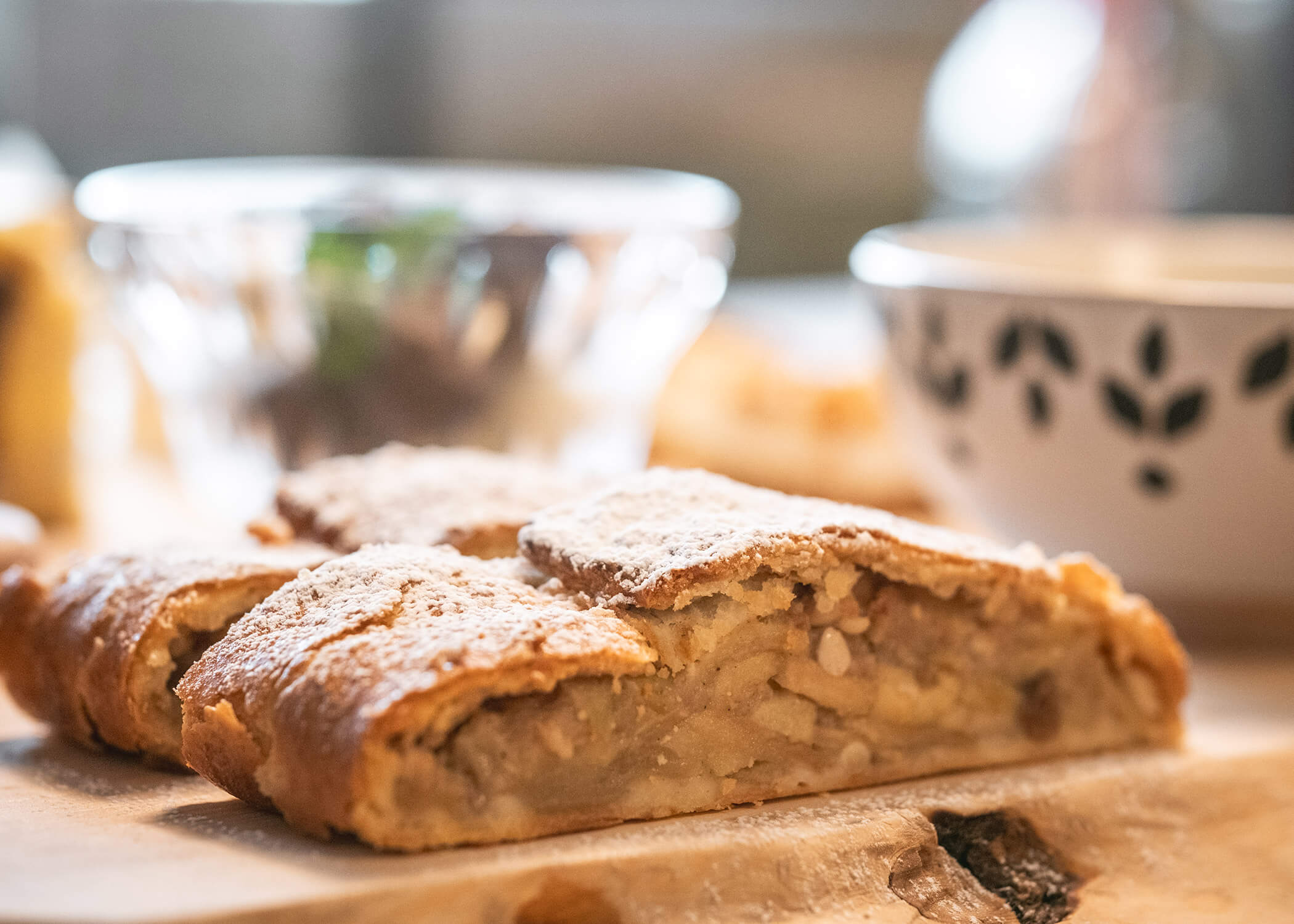 Eine Nahaufnahme von in Scheiben geschnittenem und mit Puderzucker bestreutem Apfelstrudel auf einem Holzbrett. - Hotel La Casies Mountain Living