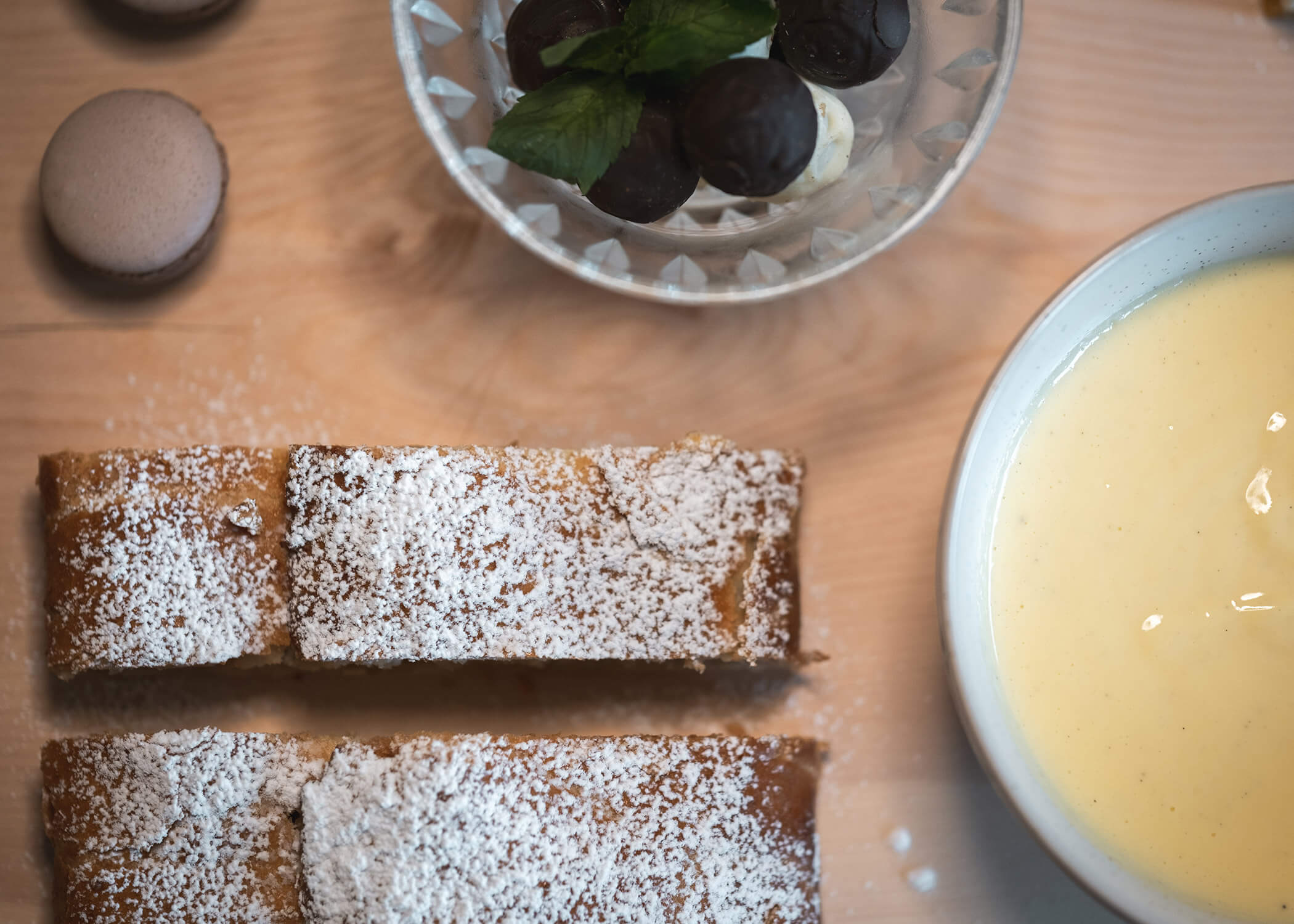 Zwei Scheiben Puderkuchen, eine Schüssel mit Pudding, Macarons und Schokoladentrüffel auf einem Holztisch. - Hotel La Casies Mountain Living