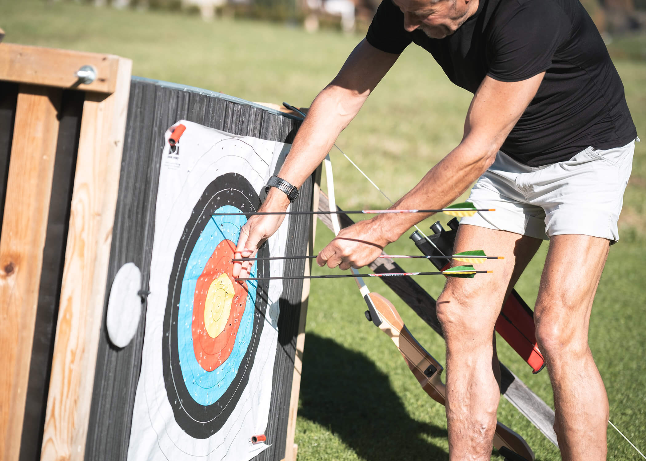 Eine Person in kurzen Hosen holt an einem sonnigen Tag Pfeile von einer Bogenschießscheibe im Freien. - Hotel La Casies Mountain Living