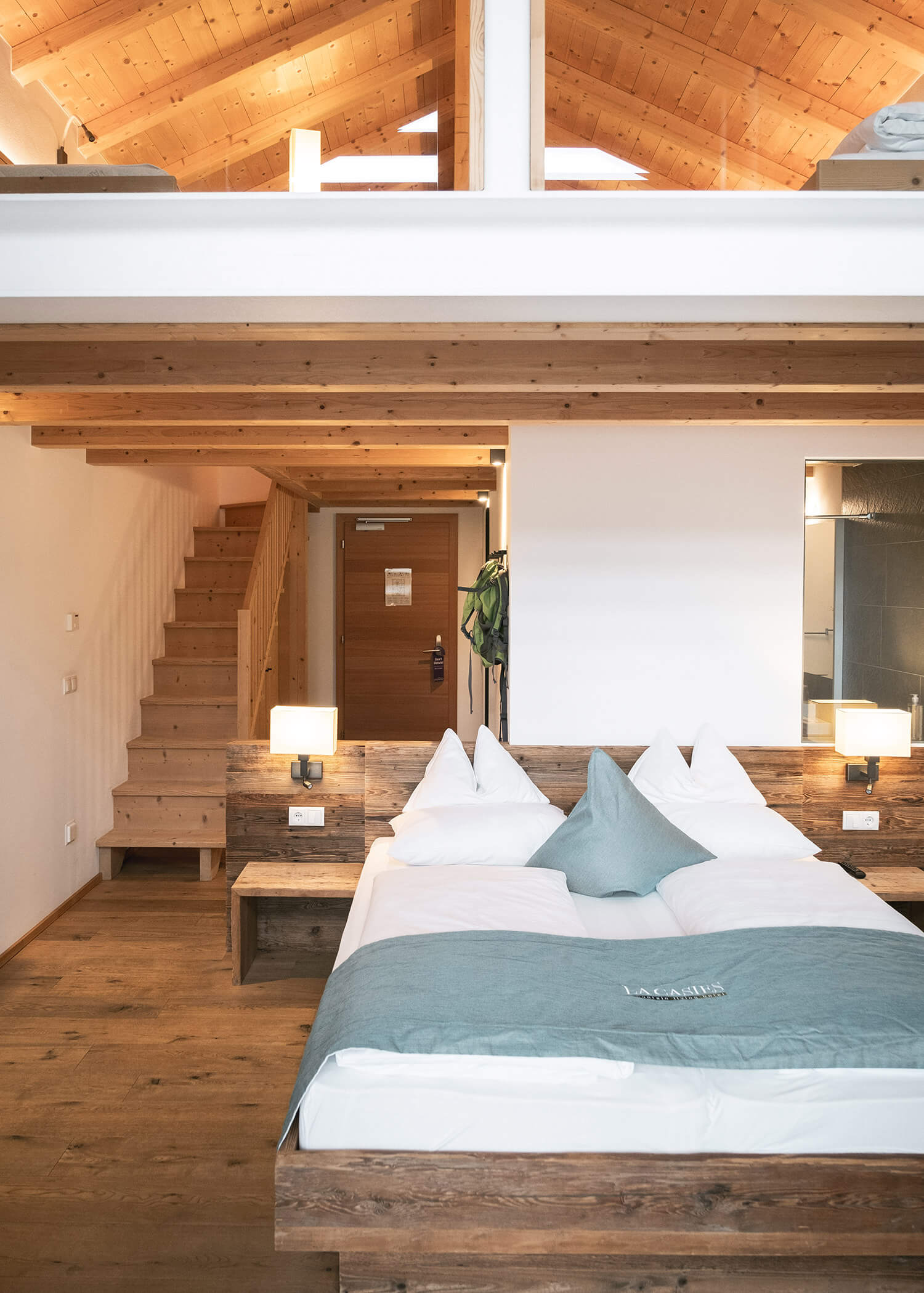 Gemütliches Schlafzimmer im Loft-Stil mit Holzdecke, Treppe und Doppelbett mit weiß-blauer Bettwäsche. - Hotel La Casies Mountain Living