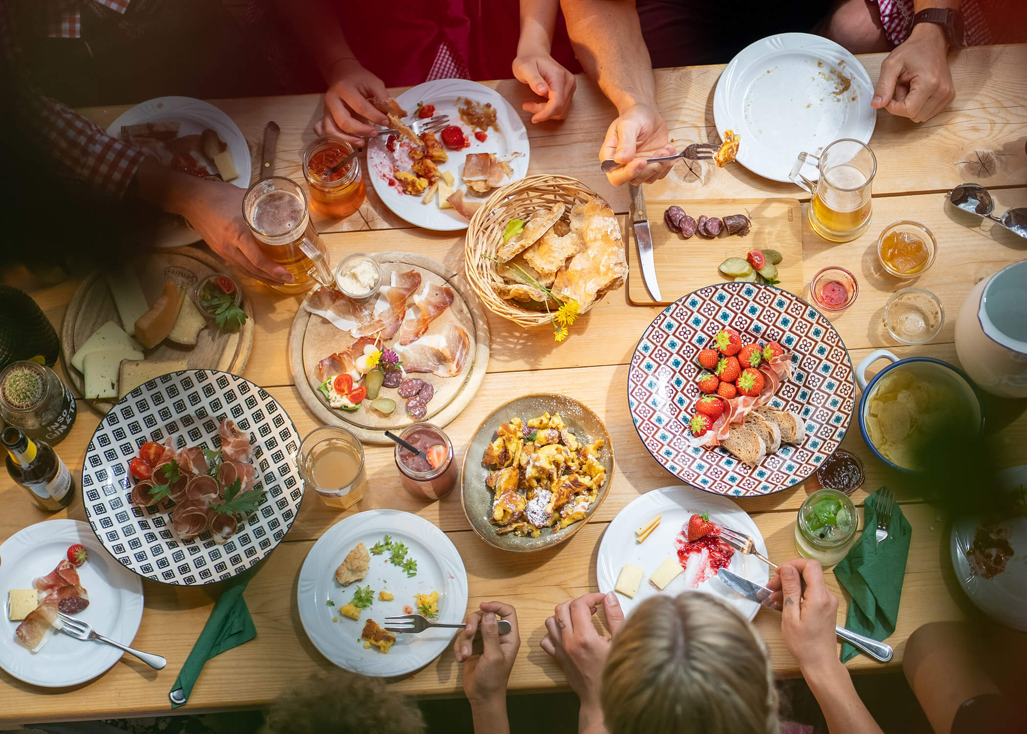 Menschen, die an einem Holztisch mit Tellern voller Essen, Brot, Obst und Getränken gemeinsam essen. - Hotel La Casies Mountain Living