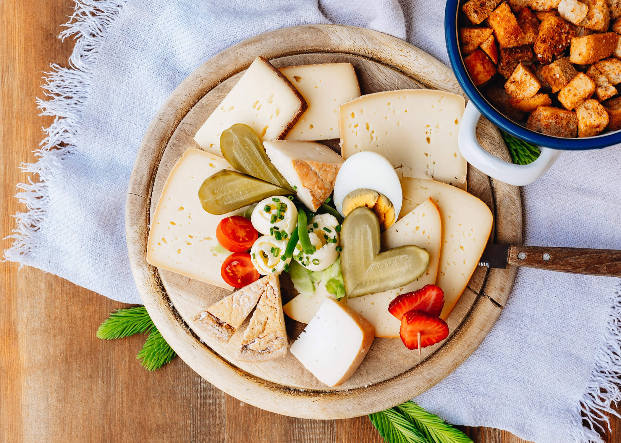 Käseplatte mit geschnittenem Käse, gekochtem Ei, Essiggurken, Tomaten und Croutons auf einem Holztisch. - Hotel La Casies Mountain Living