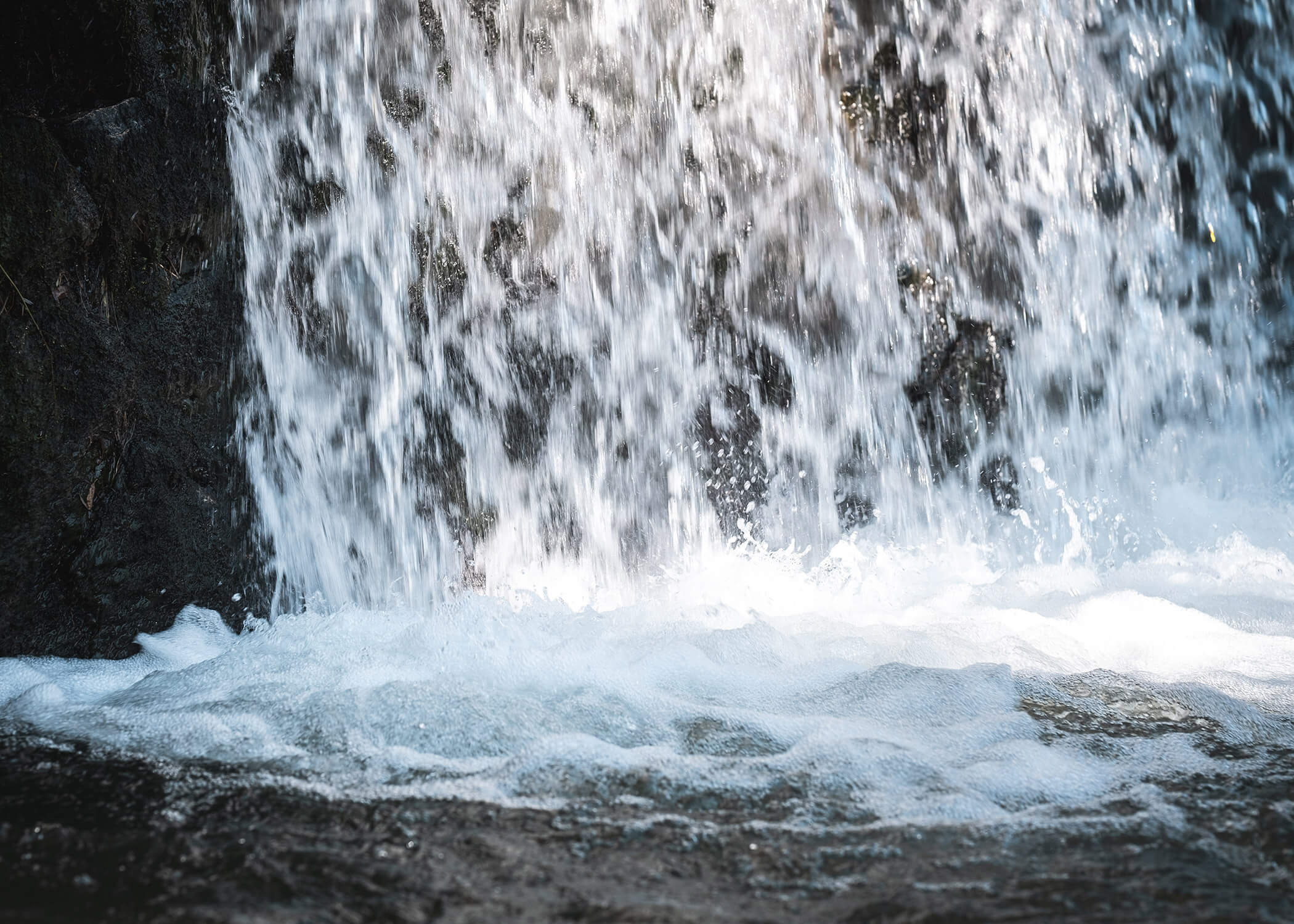 Nahaufnahme von Wasser, das in Kaskaden einen Wasserfall hinabstürzt und dabei Spritzer und weißen Schaum am Boden erzeugt. - Hotel La Casies Mountain Living