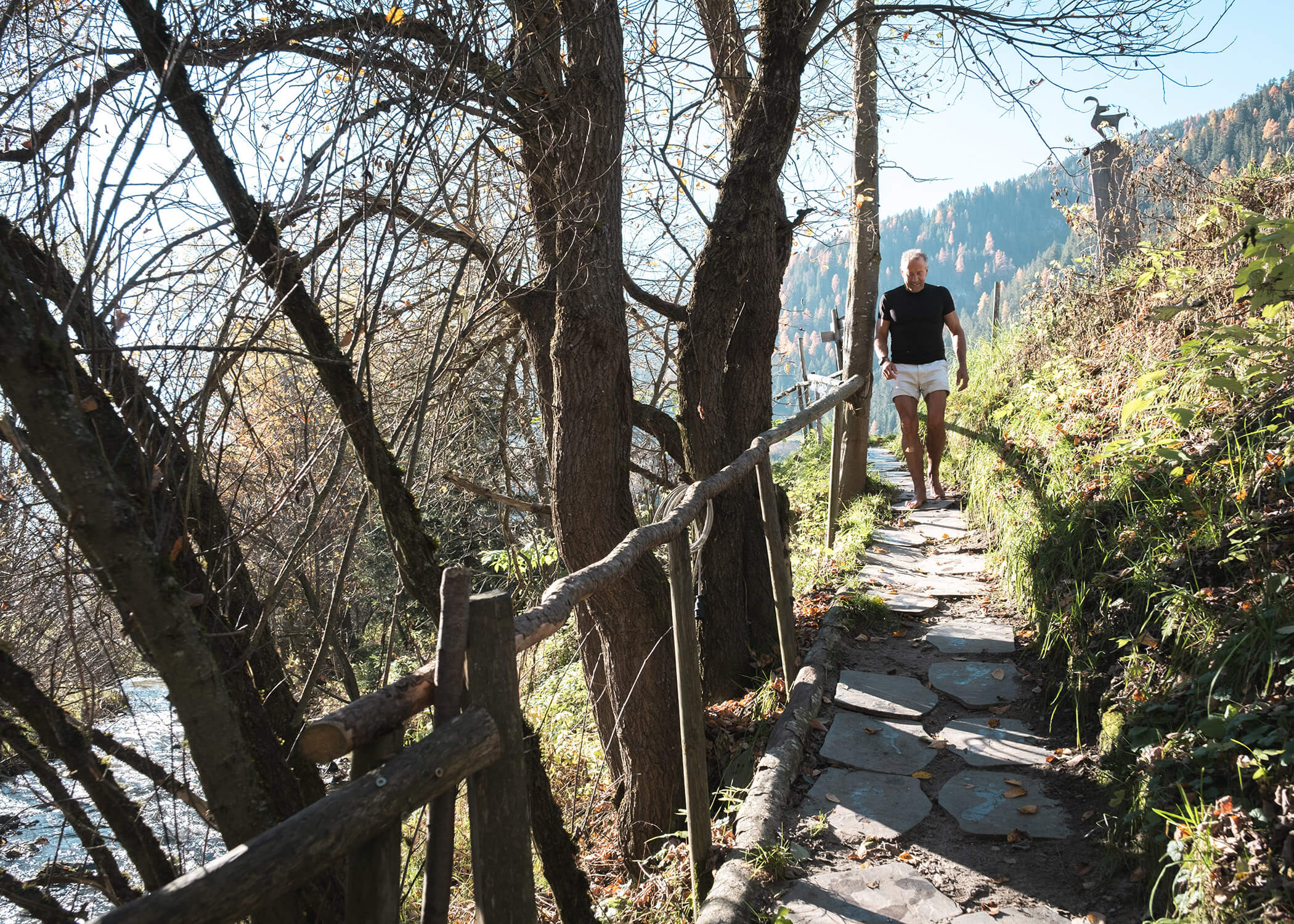 Mann geht auf einem felsigen Waldweg mit Holzgeländer, umgeben von Bäumen und Herbstlaub. - Hotel La Casies Mountain Living