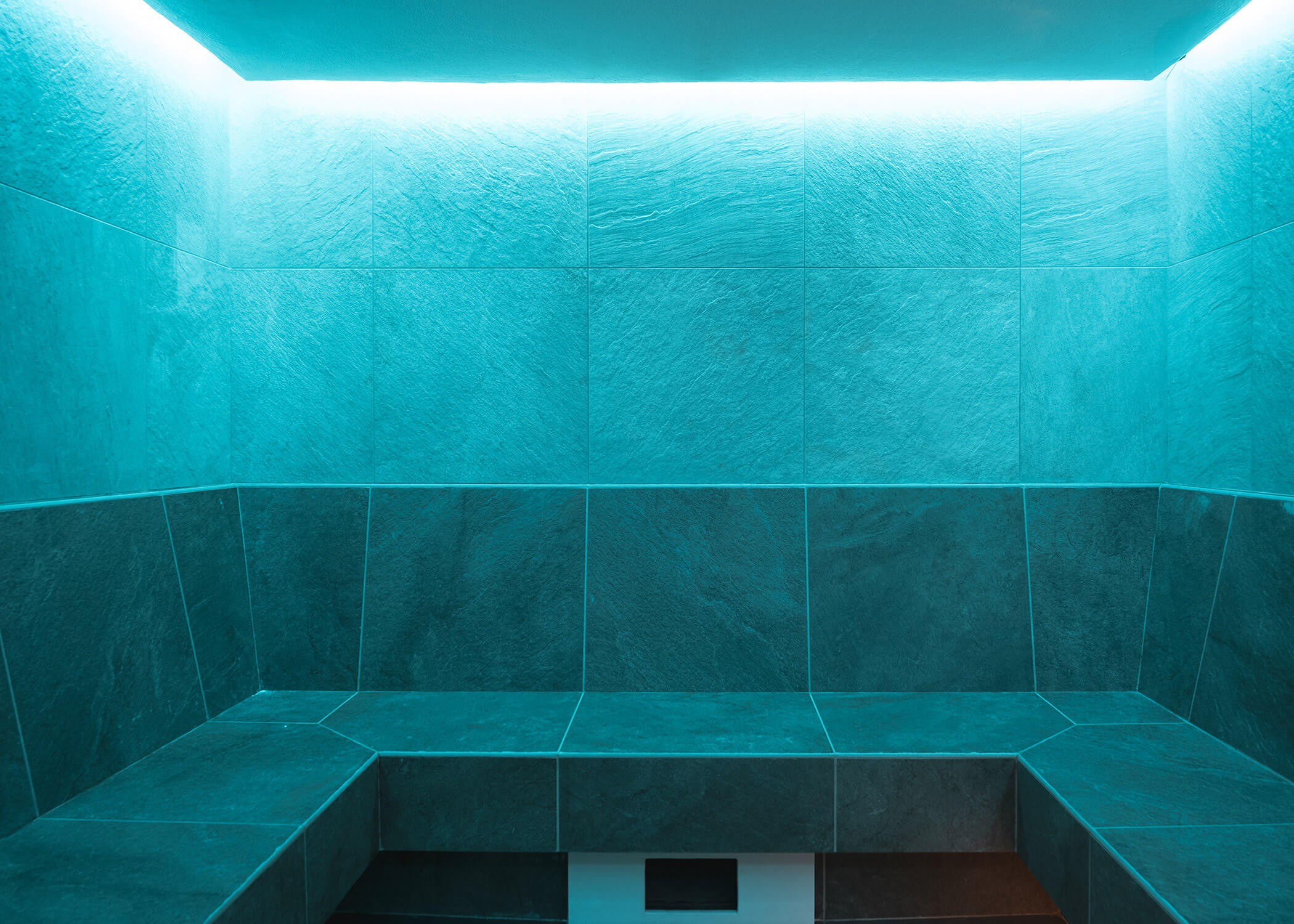 Modern gefliestes Dampfbad mit blauer Beleuchtung und eingebauten Sitzbänken an den Wänden. - Hotel La Casies Mountain Living