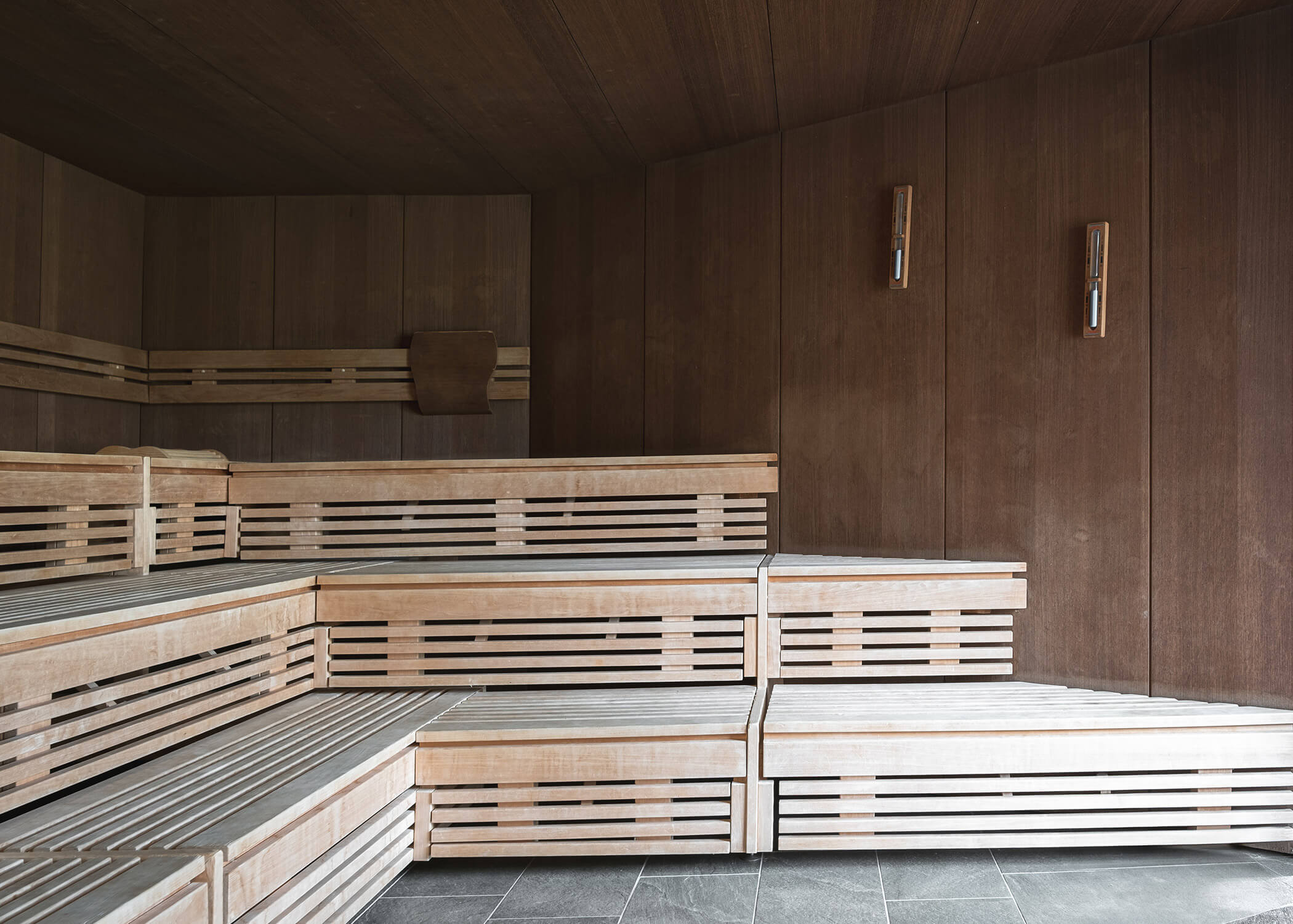 Moderne Holzsauna mit abgestuften Sitzbänken und holzgetäfelten Wänden, beleuchtet von Wandleuchten. - Hotel La Casies Mountain Living
