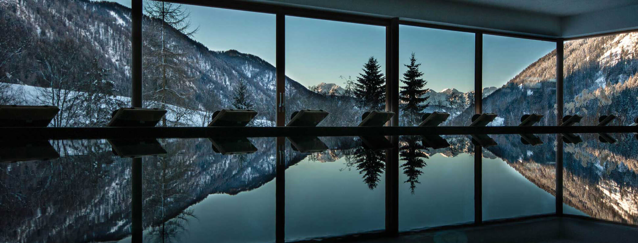 Große Fenster zeigen verschneite Berge und Bäume, die sich in einem ruhigen Hallenbad spiegeln. - Hotel La Casies Mountain Living