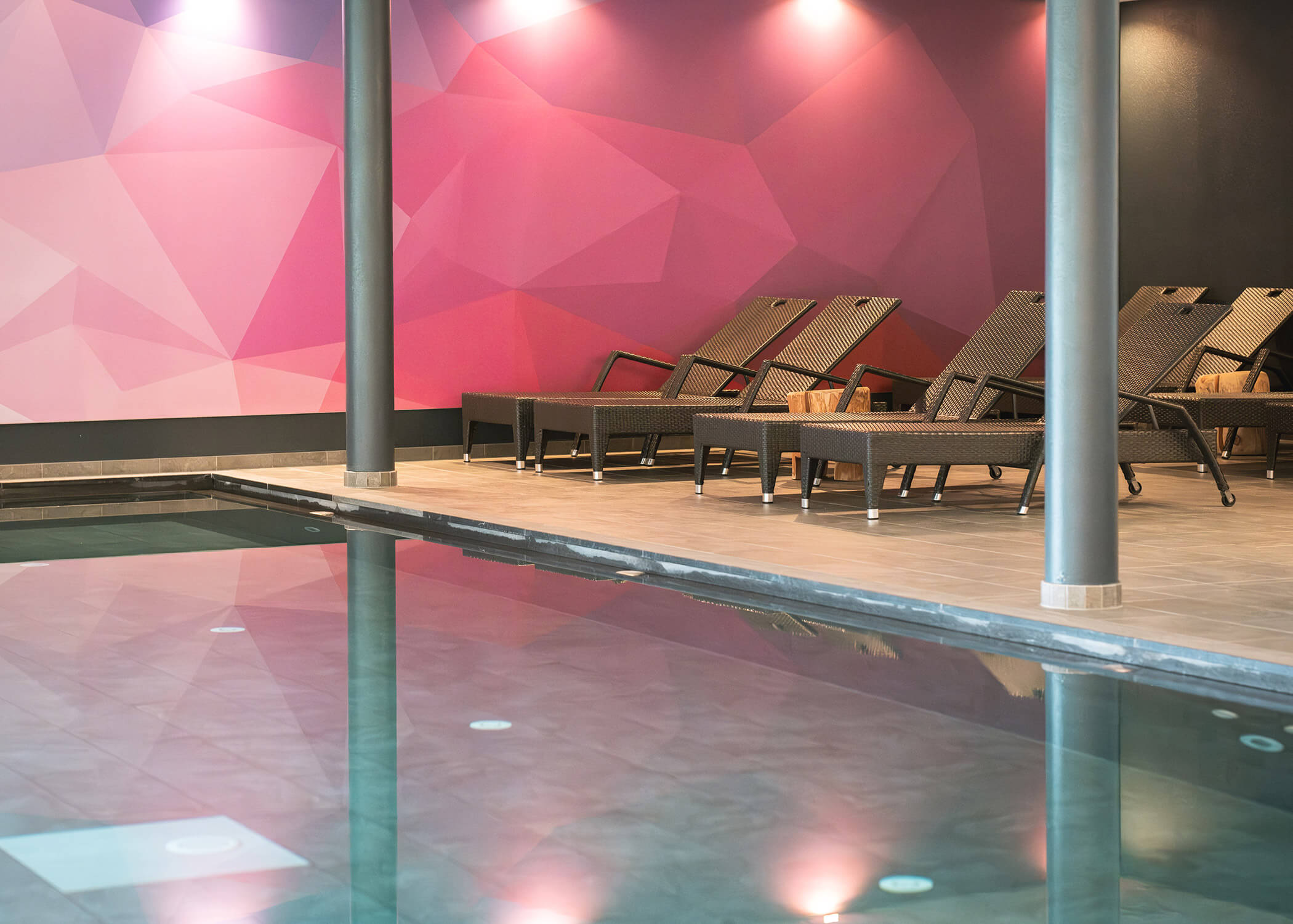 Innenpool mit Liegestühlen und einer geometrischen rosa Wandmalerei im Hintergrund. - Hotel La Casies Mountain Living