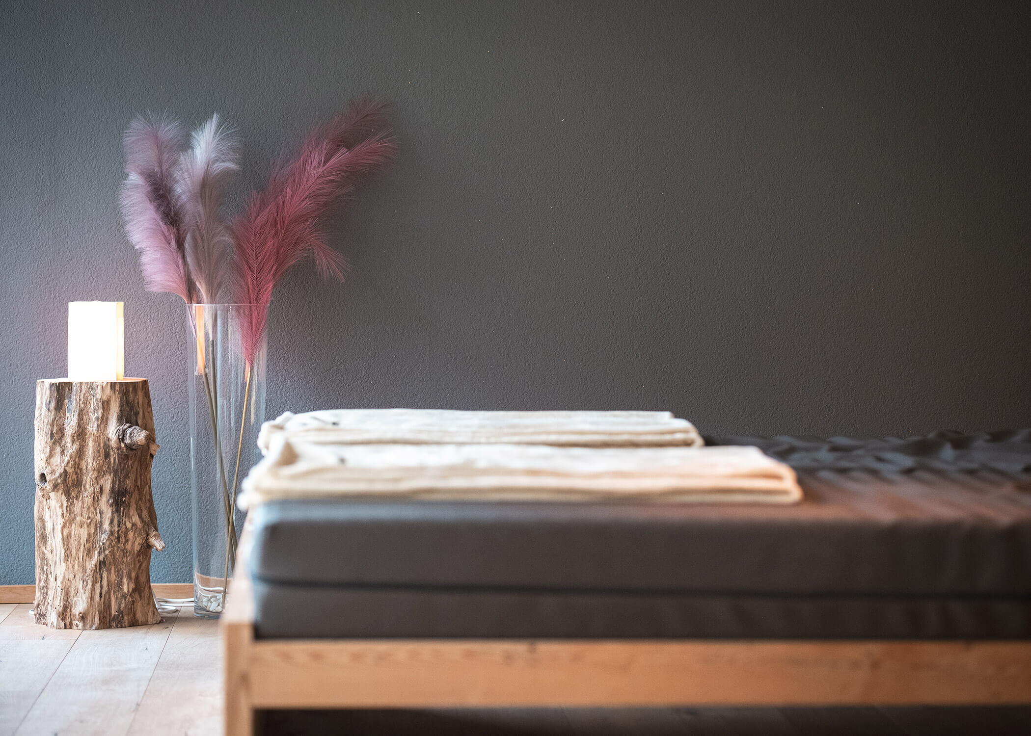 Minimalistisches Spa-Setting mit gefalteten Handtüchern auf einem Bett, sanftem Licht und dekorativen Federn in einer Vase. - Hotel La Casies Mountain Living