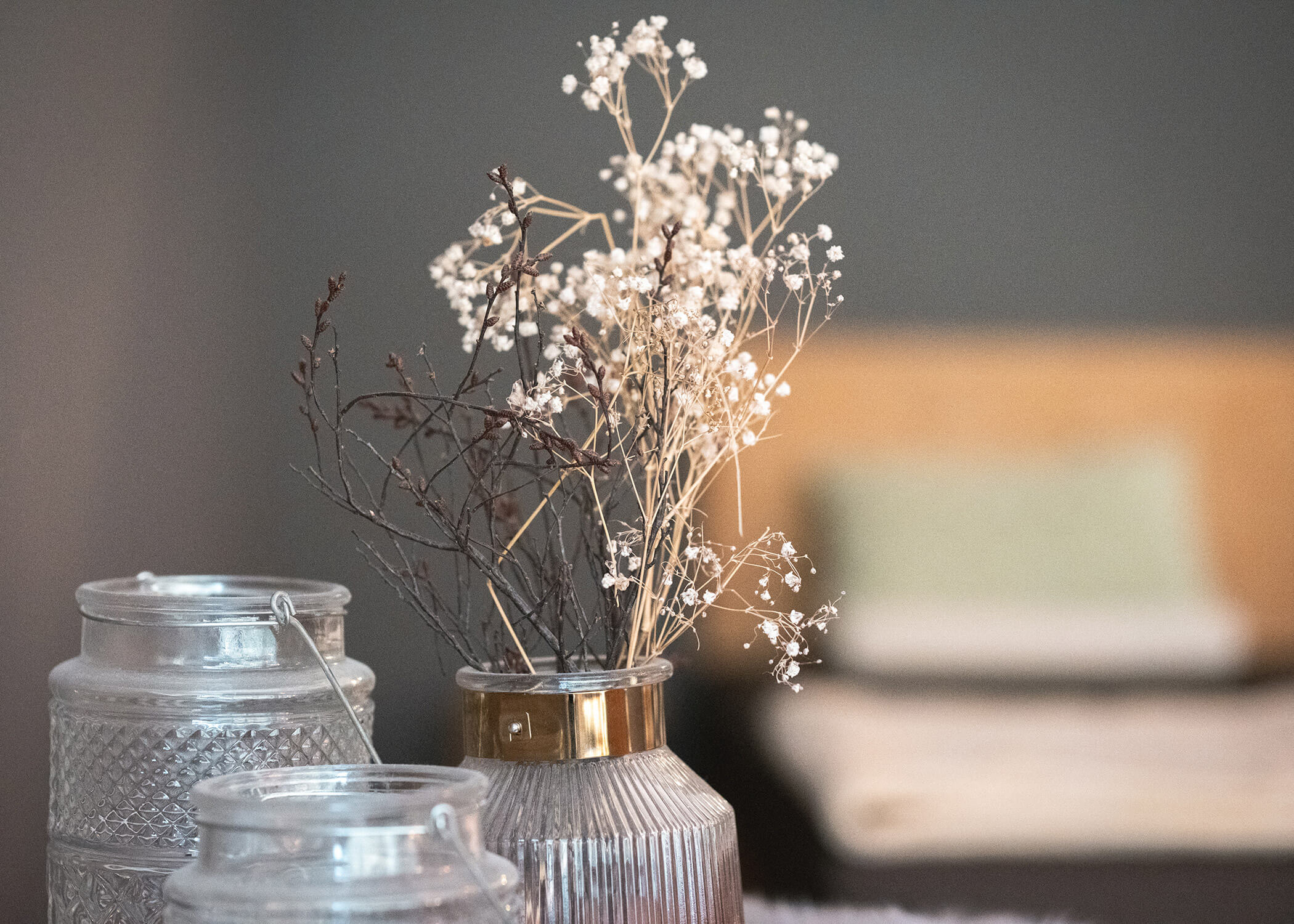 Glasgefäß mit getrockneten Blumen und zwei leeren Glasbehältern vor einem unscharfen Hintergrund. - Hotel La Casies Mountain Living