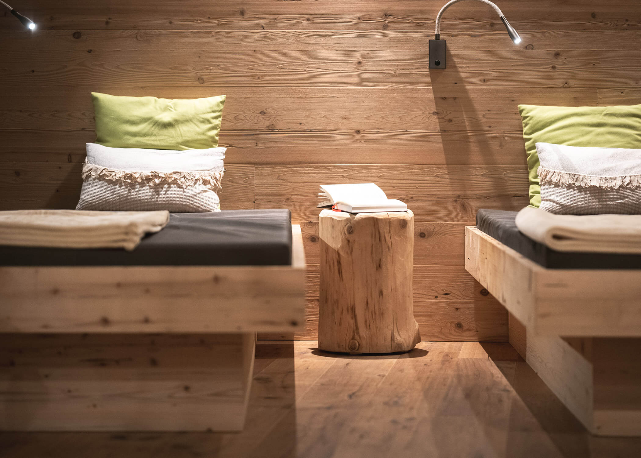 Zwei Holzbetten mit grünen Kissen und Decken, getrennt durch einen kleinen Holztisch mit einem offenen Buch. - Hotel La Casies Mountain Living