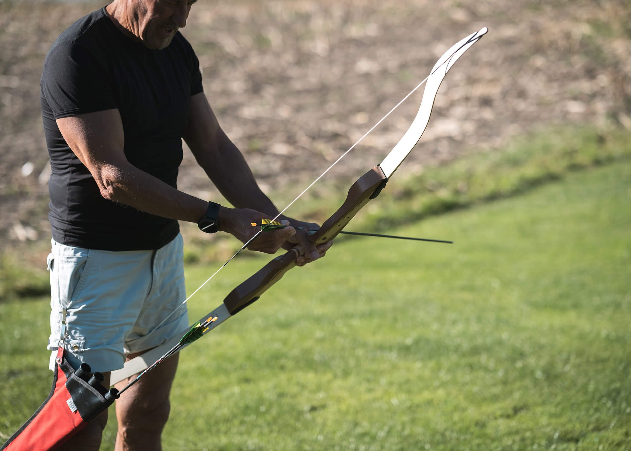 Eine Person im Freien, die einen Pfeil auf einen hölzernen Bogen lädt, steht im Gras und hat einen Köcher an der Seite. - Hotel La Casies Mountain Living