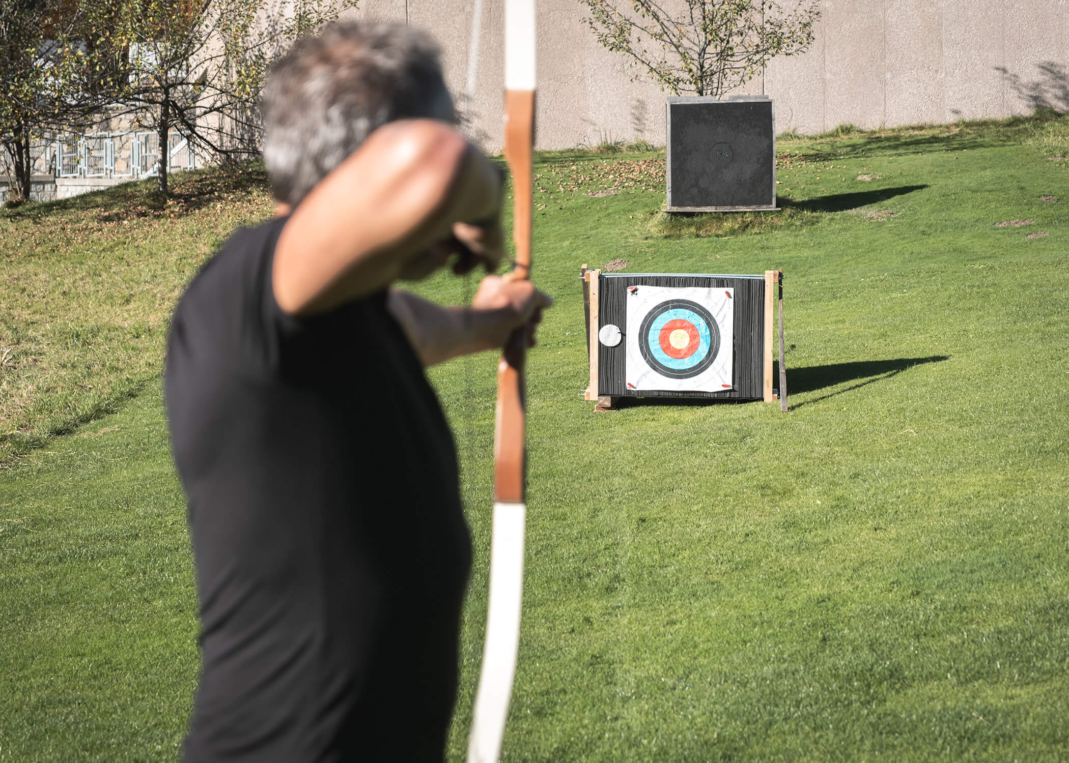 Eine Person zielt mit einem Bogen auf eine Zielscheibe, die bei Tageslicht auf einer Wiese aufgestellt ist. - Hotel La Casies Mountain Living