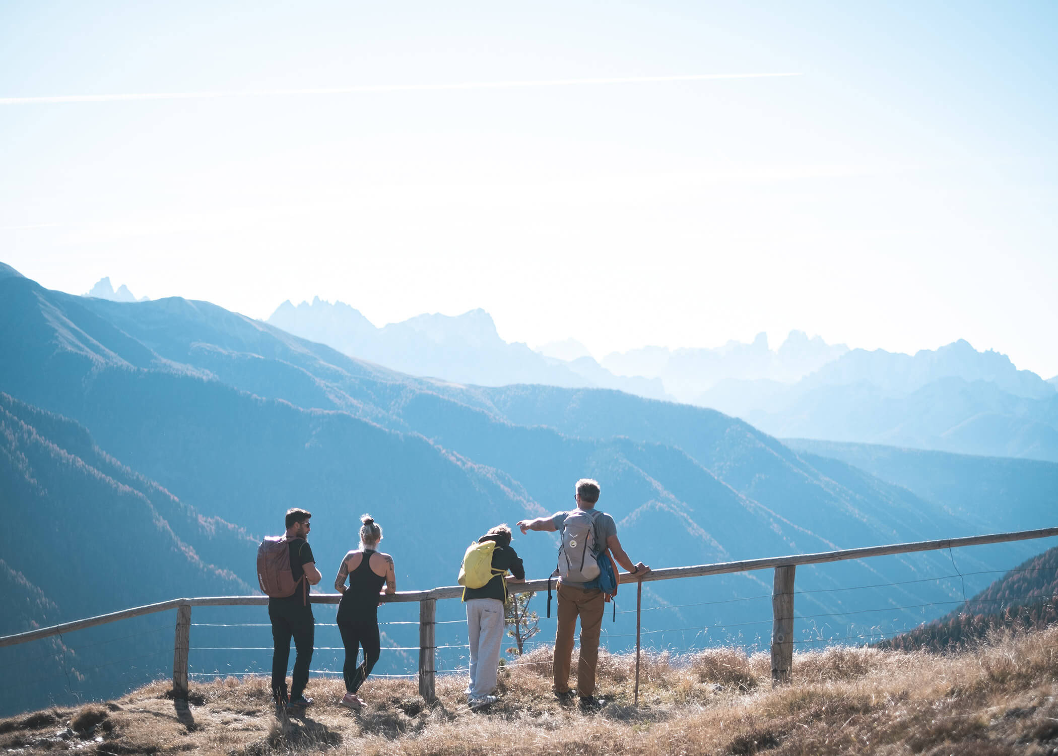 Vier Wanderer stehen an einem Holzzaun und blicken auf blaue Bergketten unter einem klaren Himmel. - Hotel La Casies Mountain Living