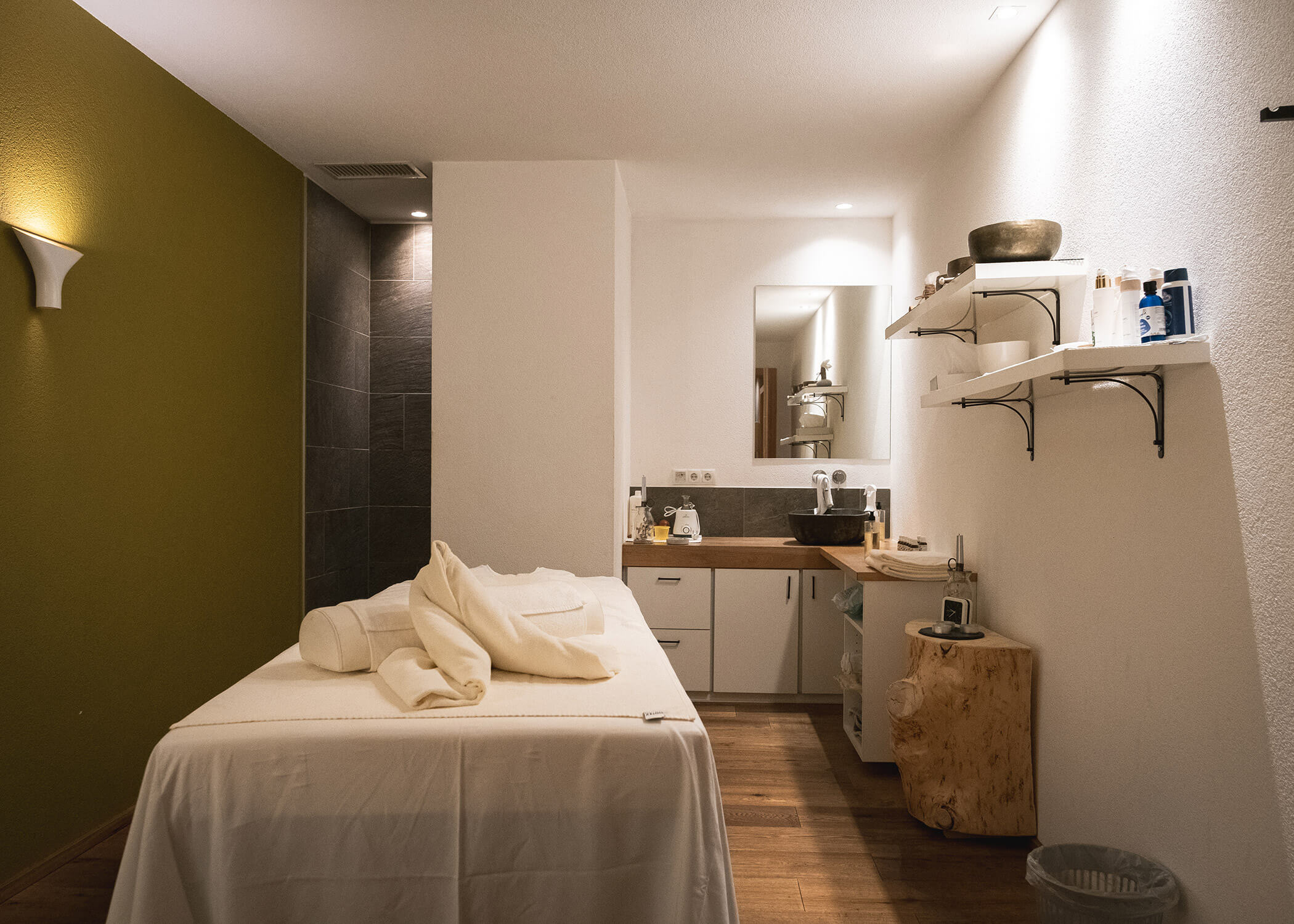 Moderner Spa-Raum mit Massageliege, Handtüchern, Regalen mit Produkten und sanfter, warmer Beleuchtung. - Hotel La Casies Mountain Living